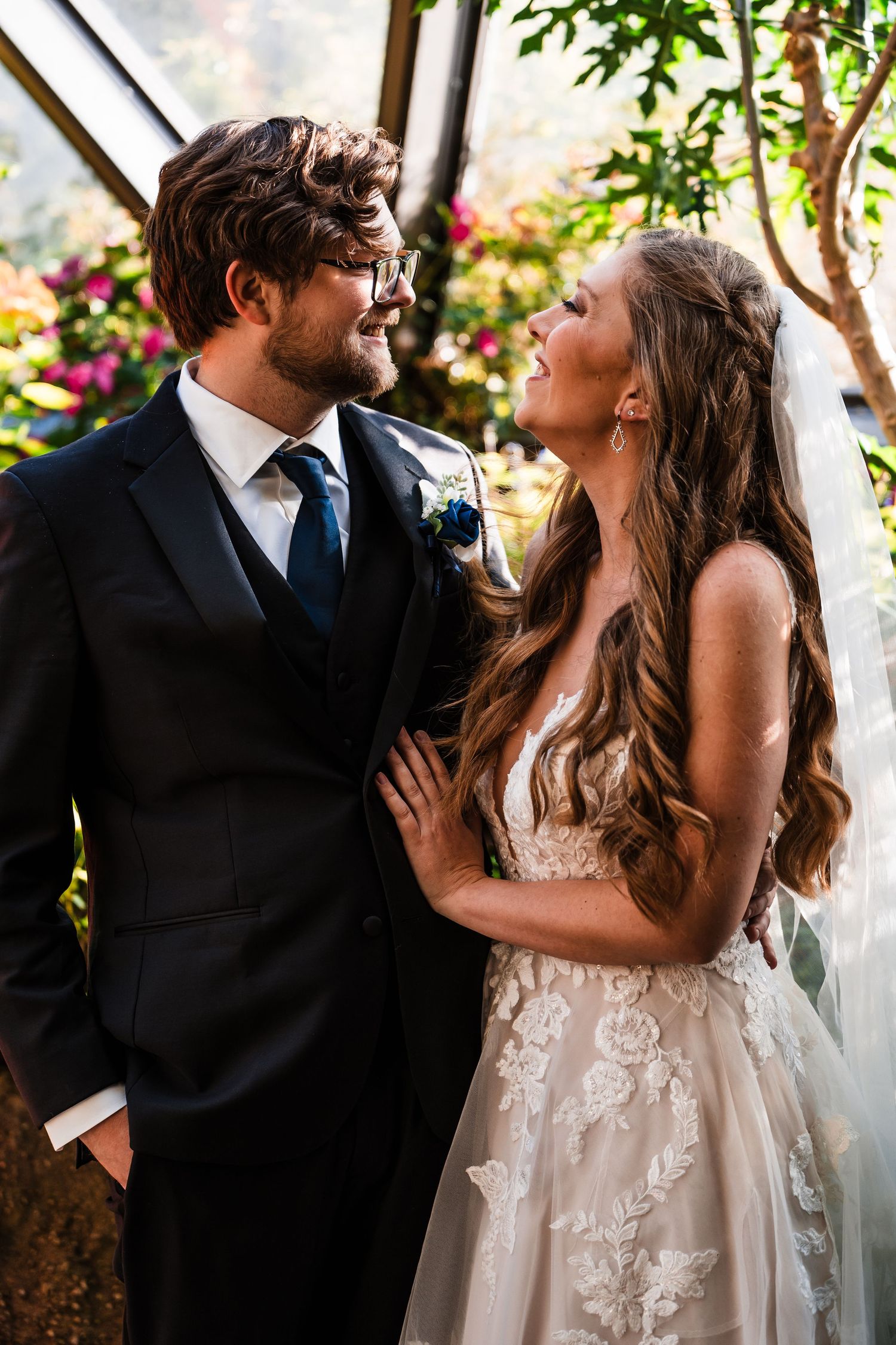 Newlyweds share an intimate moment surrounded by flowers in a greenhouse setting.