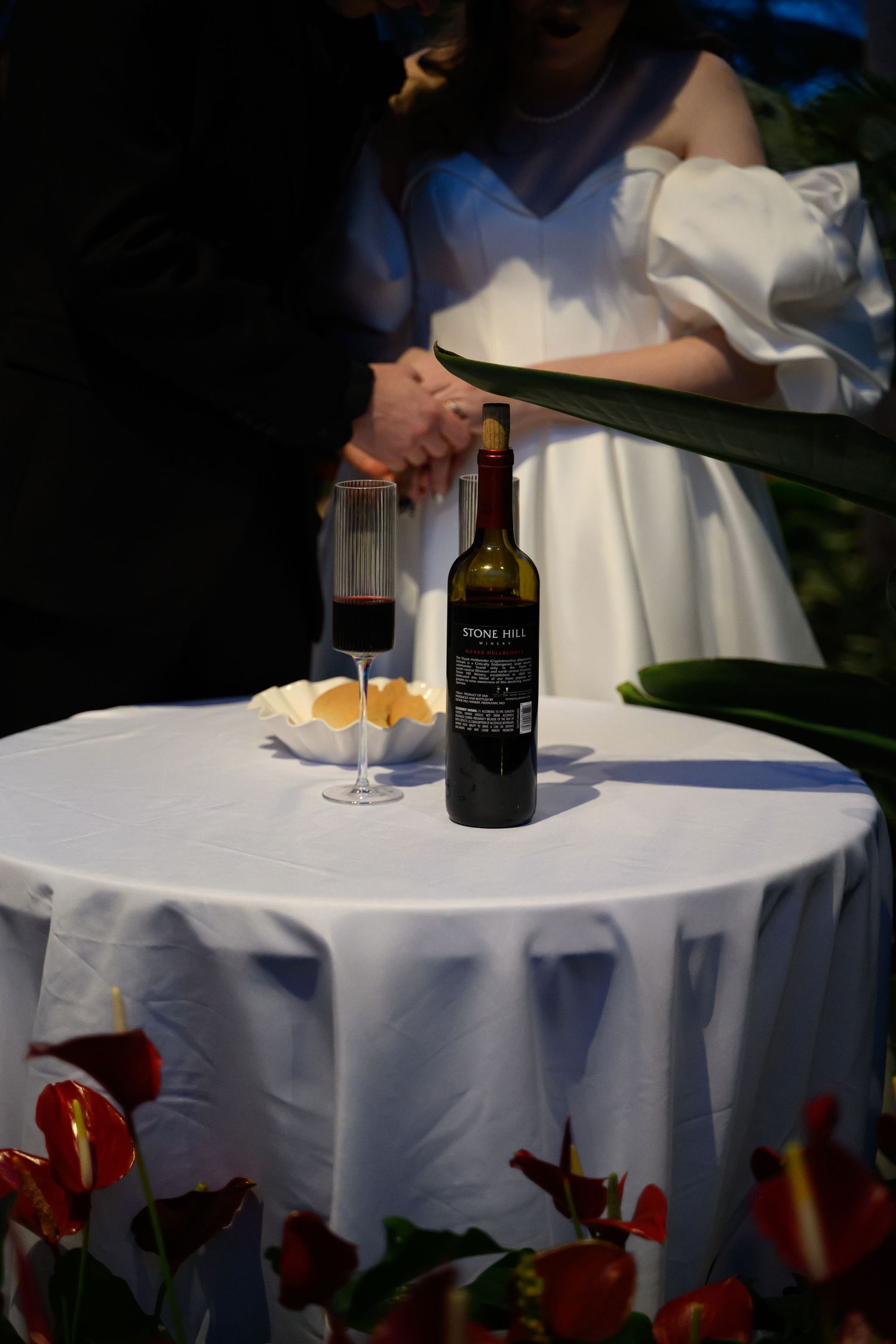 A wine bottle and glasses set on a white tablecloth during a wedding celebration.