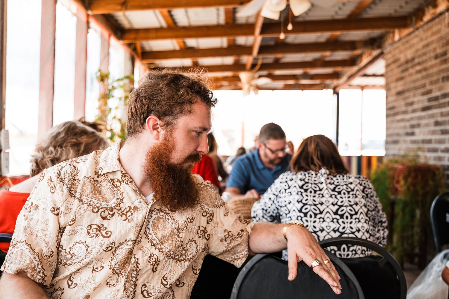 Inside a rustic brick venue with wooden beams, people socialize at a casual gathering.