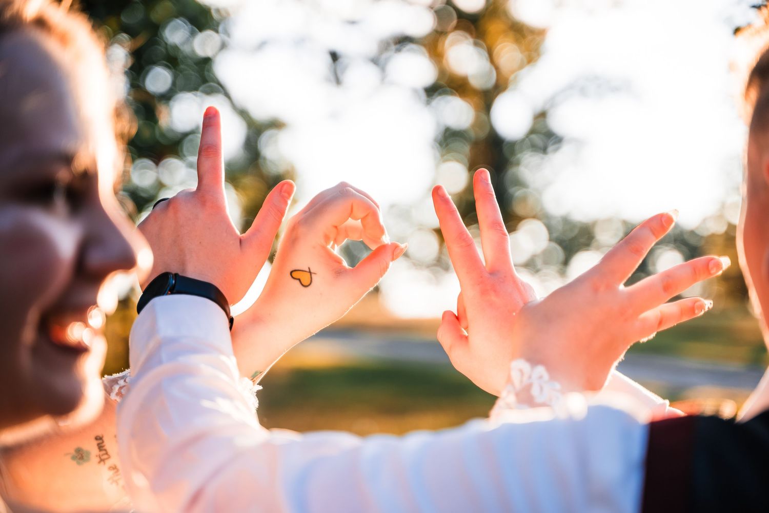 Two hands making a heart shape with rings in golden sunlight at a wedding ceremony.