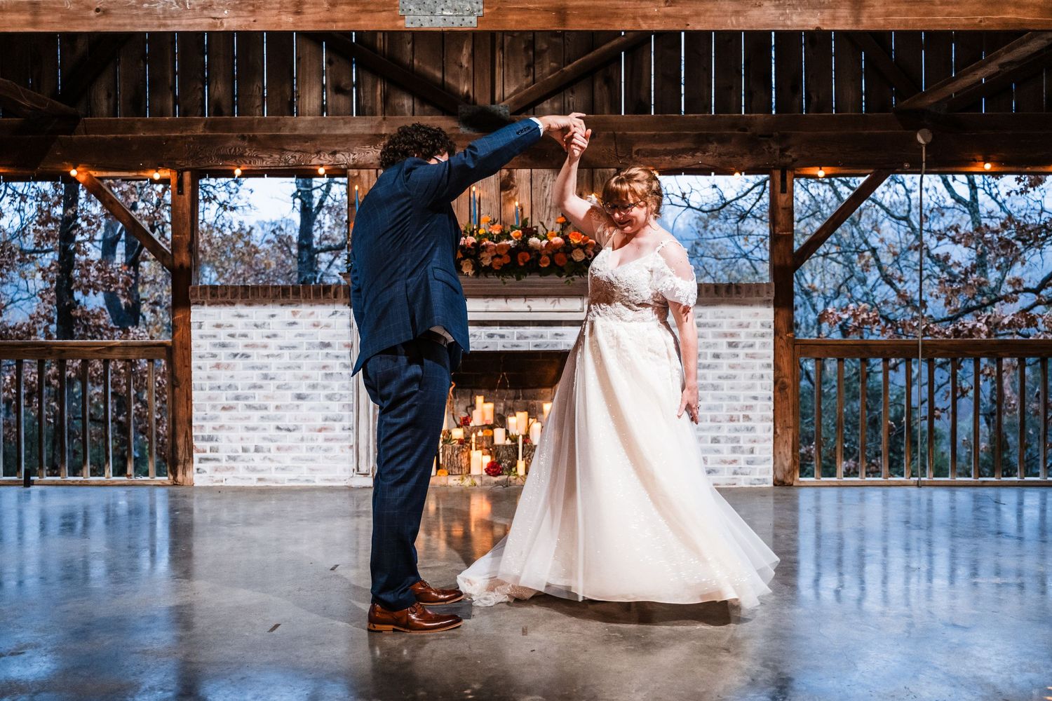 Dancing couple twirls during first dance in rustic venue with string lights.