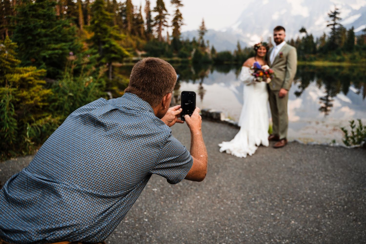 A photographer captures wedding moments with mountain peaks and evergreen trees in the background.
