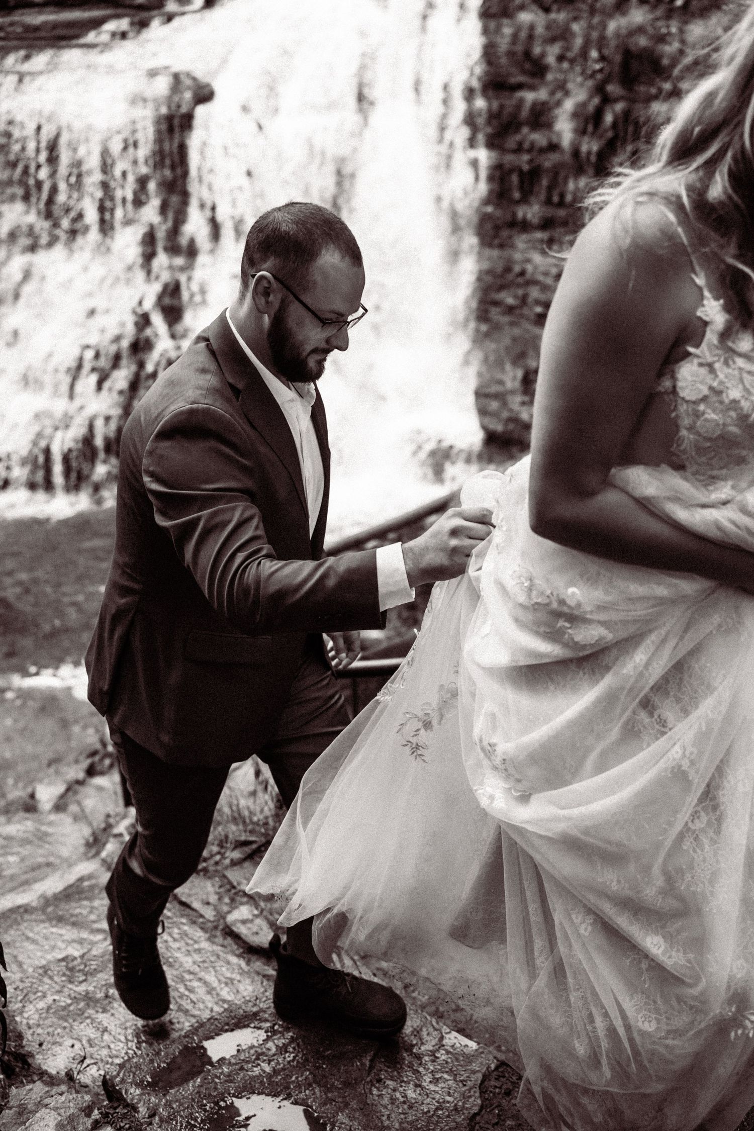 A couple shares an intimate moment by a cascading waterfall during their wedding photoshoot.