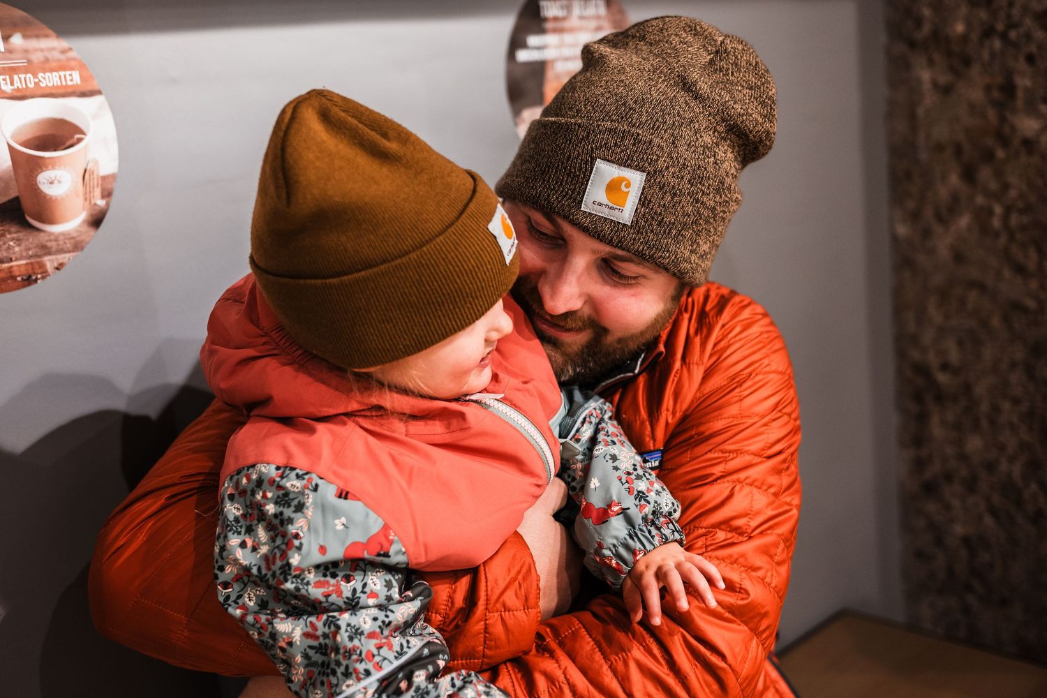 A couple in orange winter coats and brown beanies share tender moments in a photo collage sequence.