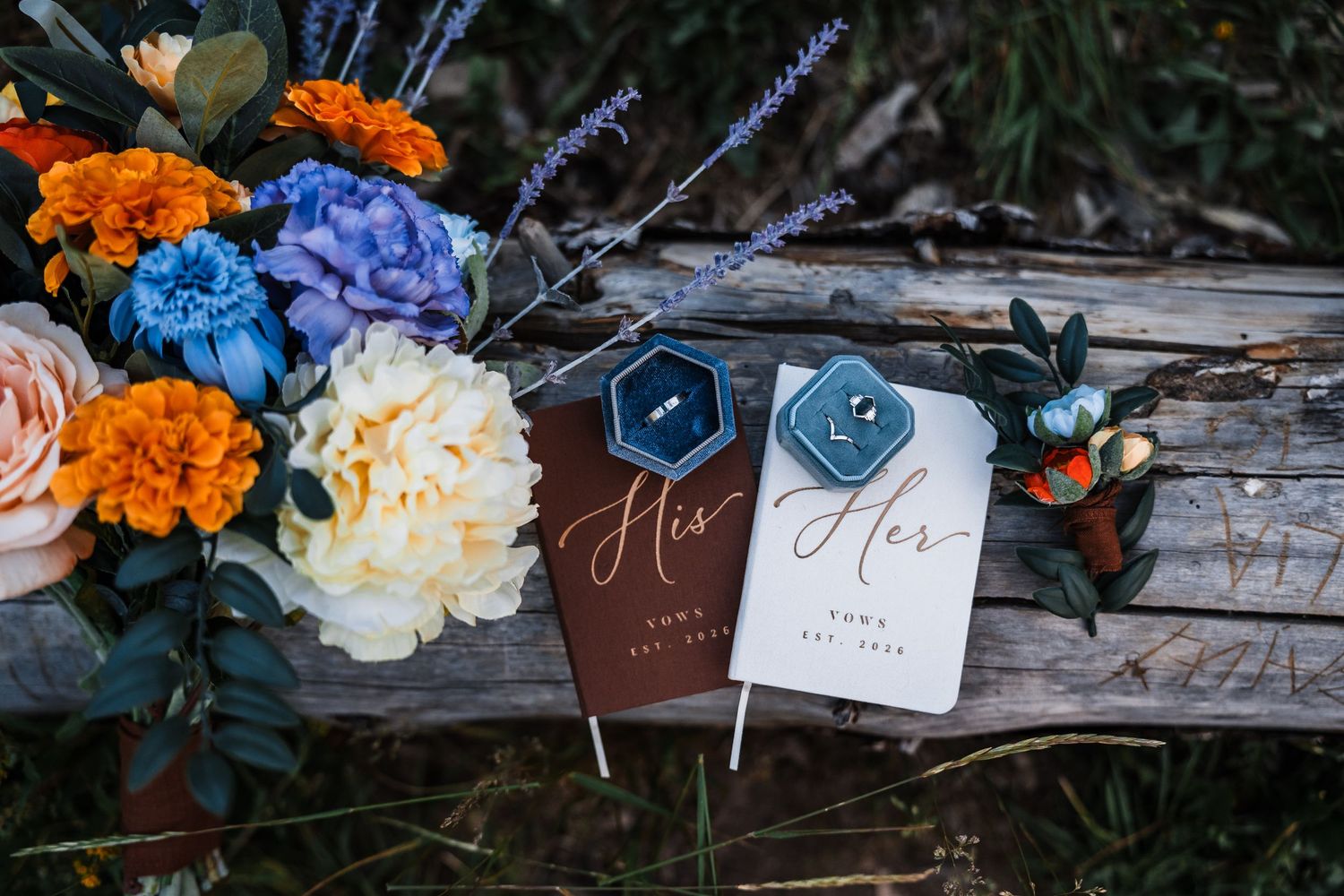 Colorful wedding flat lay with his and her vow books, ring boxes, boutonniere, and vibrant floral bouquet.