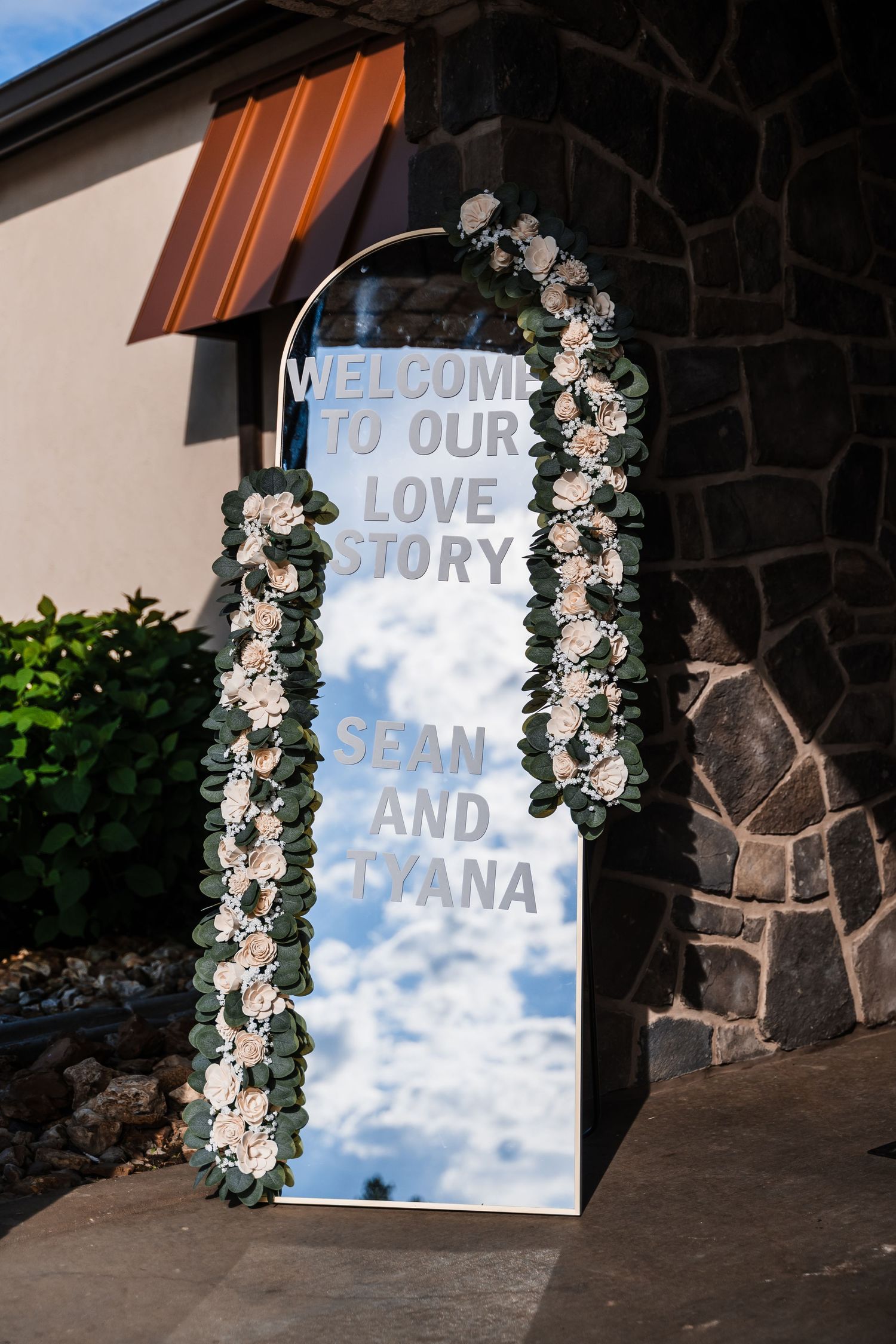 Mirror wedding welcome sign with floral arch reading Welcome To Our Love Story Sean and Lyana.