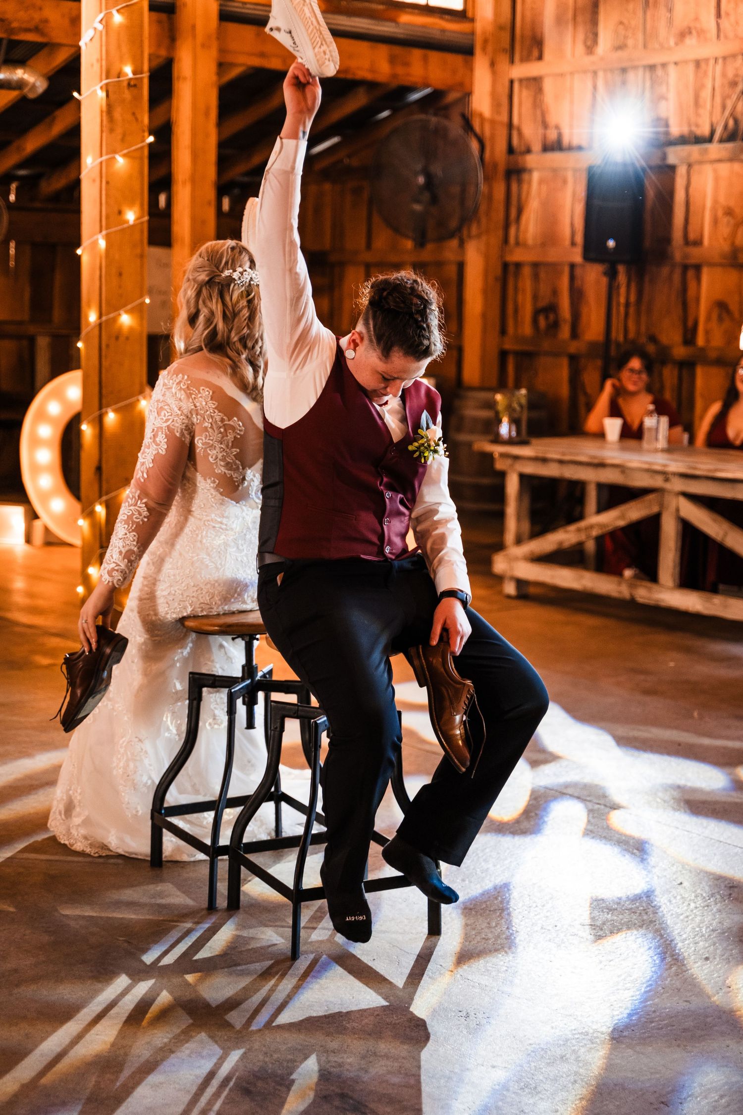 A couple dances at their rustic barn wedding reception with string lights and wooden decor in warm lighting.