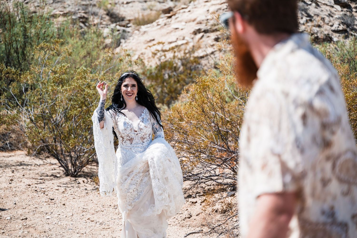 Bride in lace dress poses in desert landscape during wedding photoshoot.