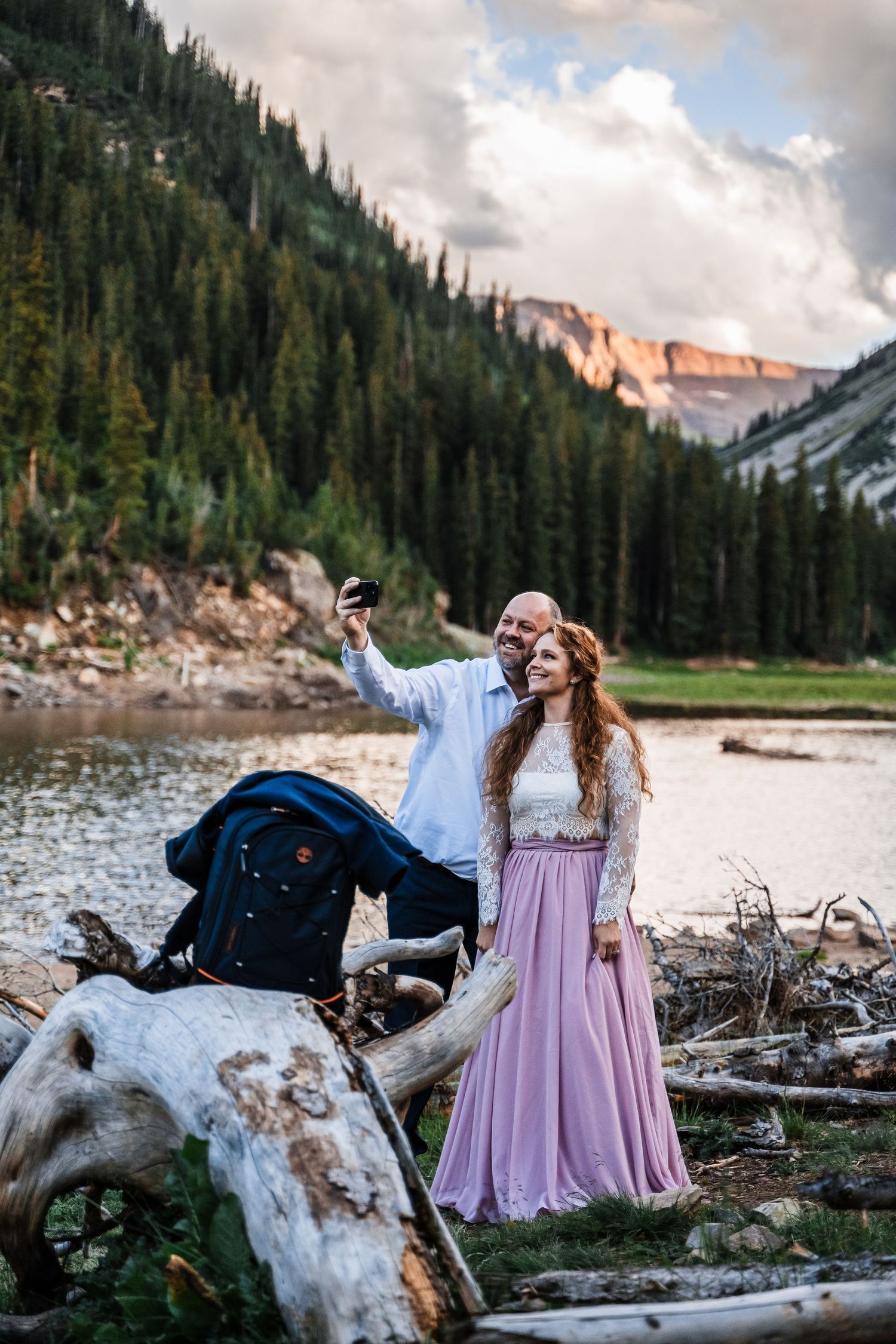 A joyful moment captured by a mountain lake with towering peaks and driftwood in the foreground.