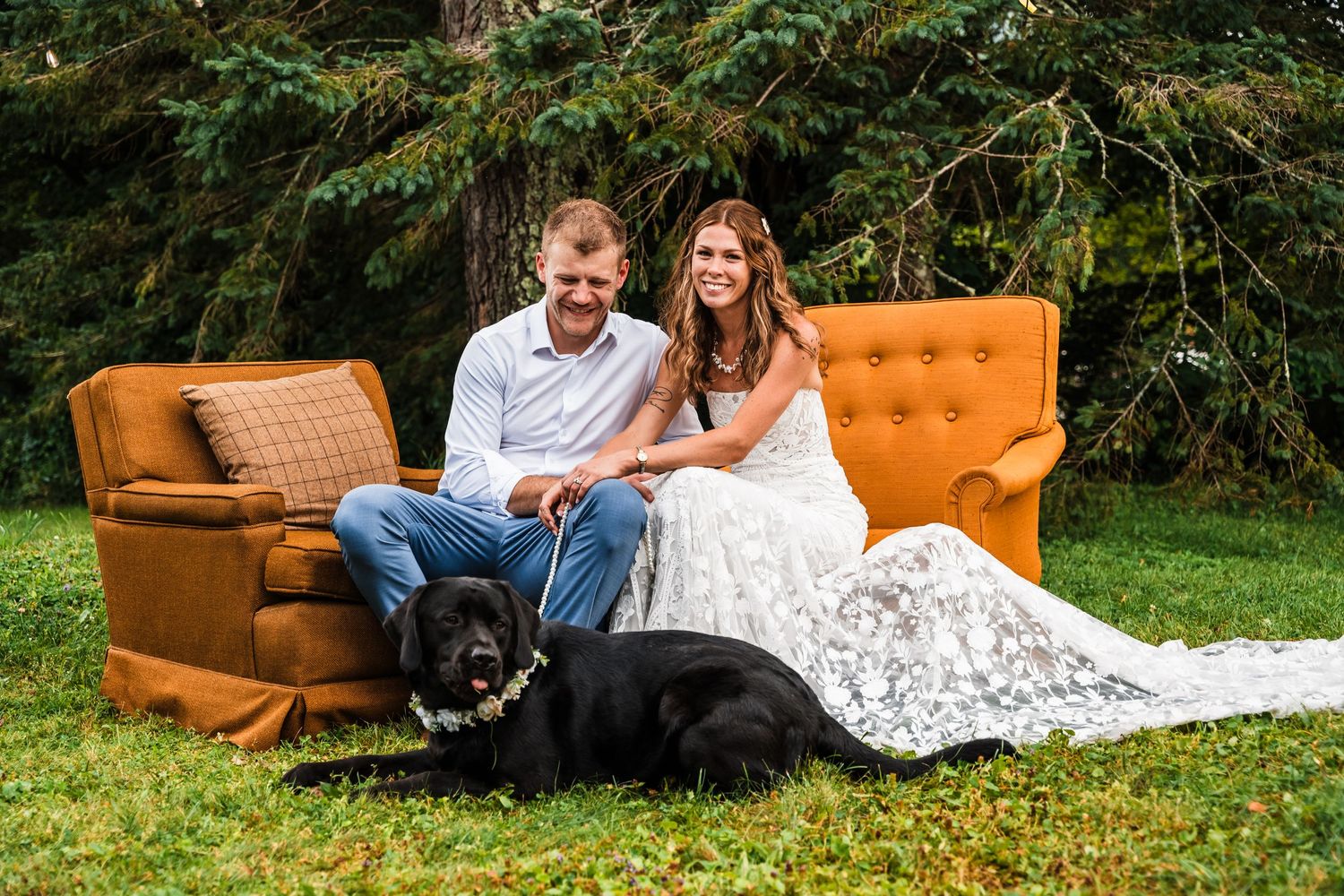 Couple relaxing on vintage orange couches with their black dog on a lawn.