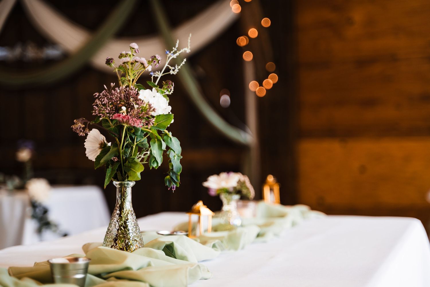 Elegant floral centerpiece with wildflowers in a glass vase on a white tablecloth.