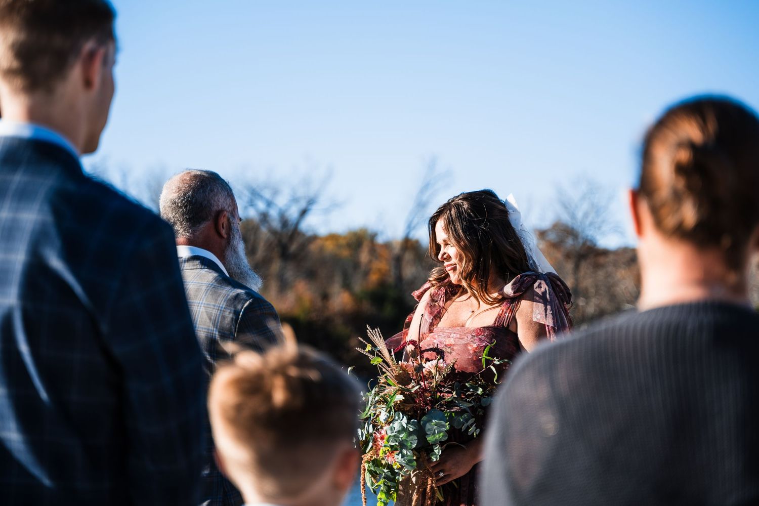 Intimate outdoor wedding ceremony taking place on a bright winter day beside a lake.
