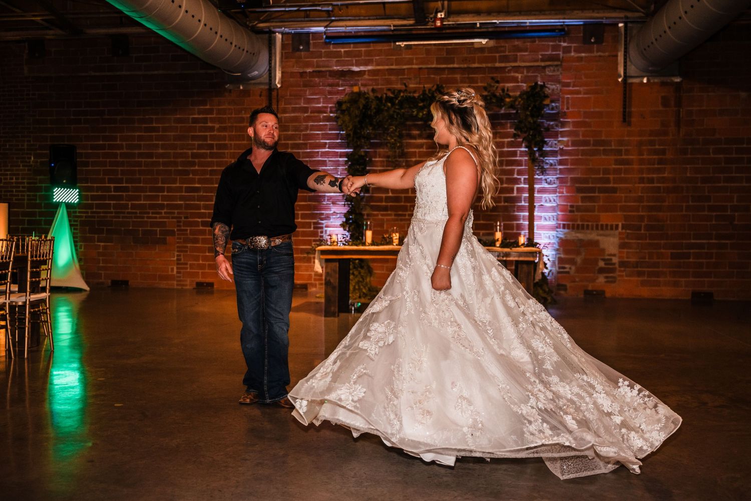 Couple dancing in an industrial brick venue with dramatic lighting and flowing white gown.