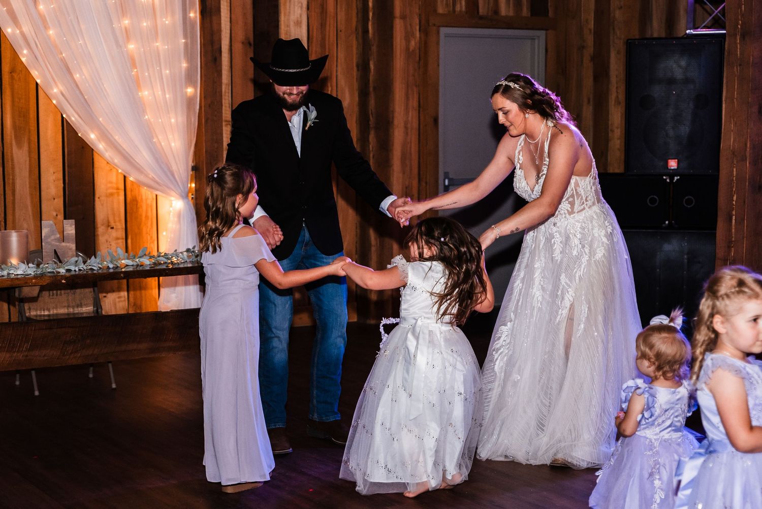 People dancing together at a rustic barn wedding reception with twinkling lights and tulle decorations.
