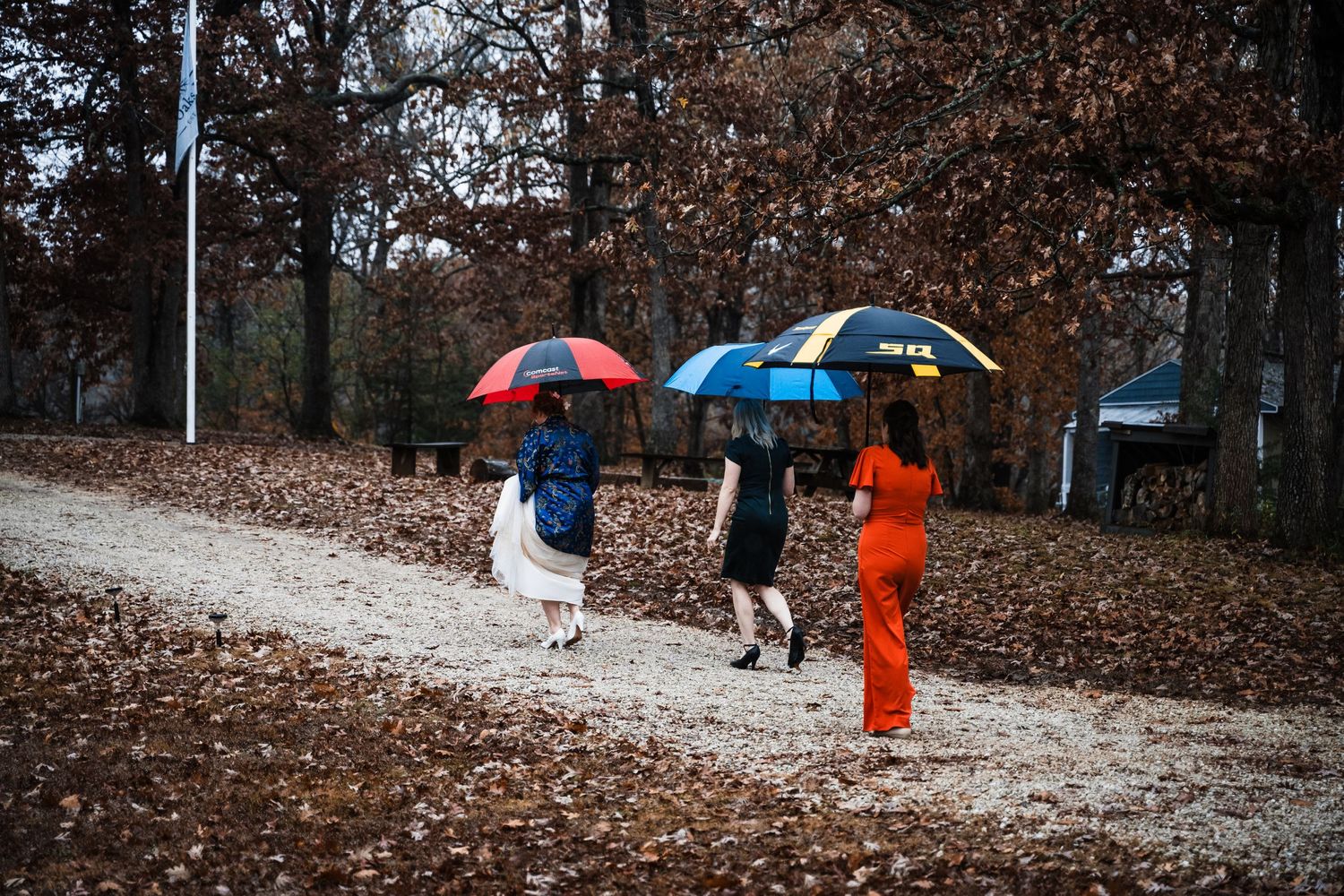 Three people with colorful umbrellas walking down a leaf-covered path in autumn.