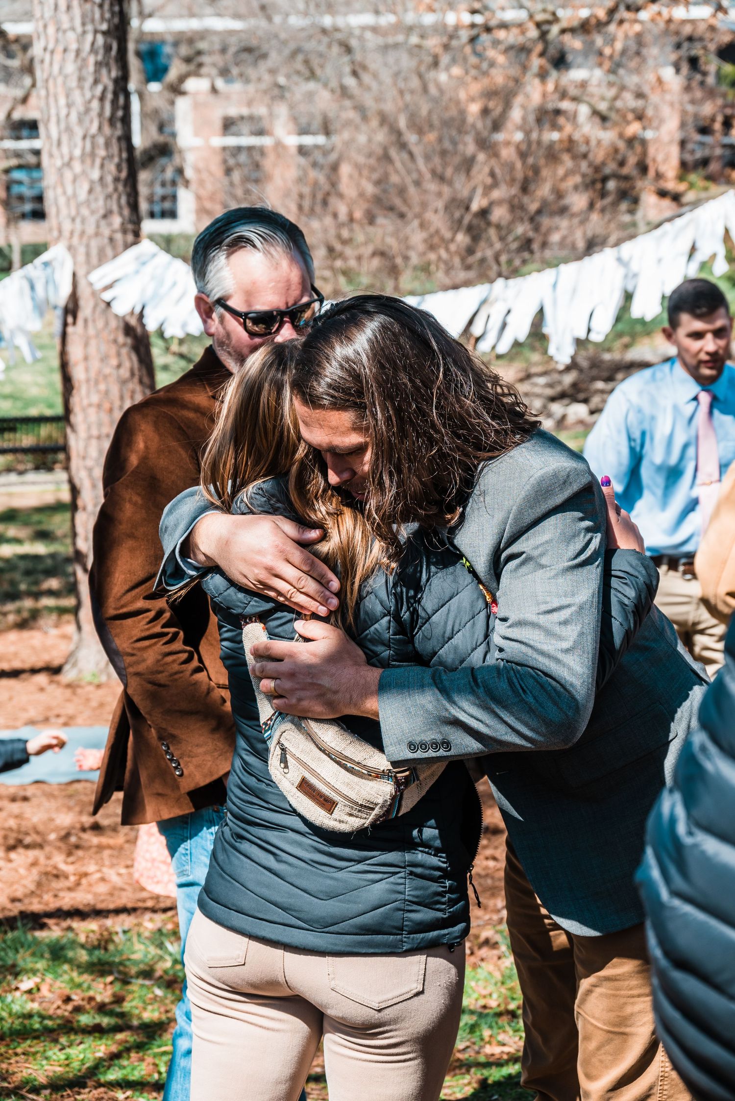 Guests embracing during an outdoor celebration beneath white fabric decorations.