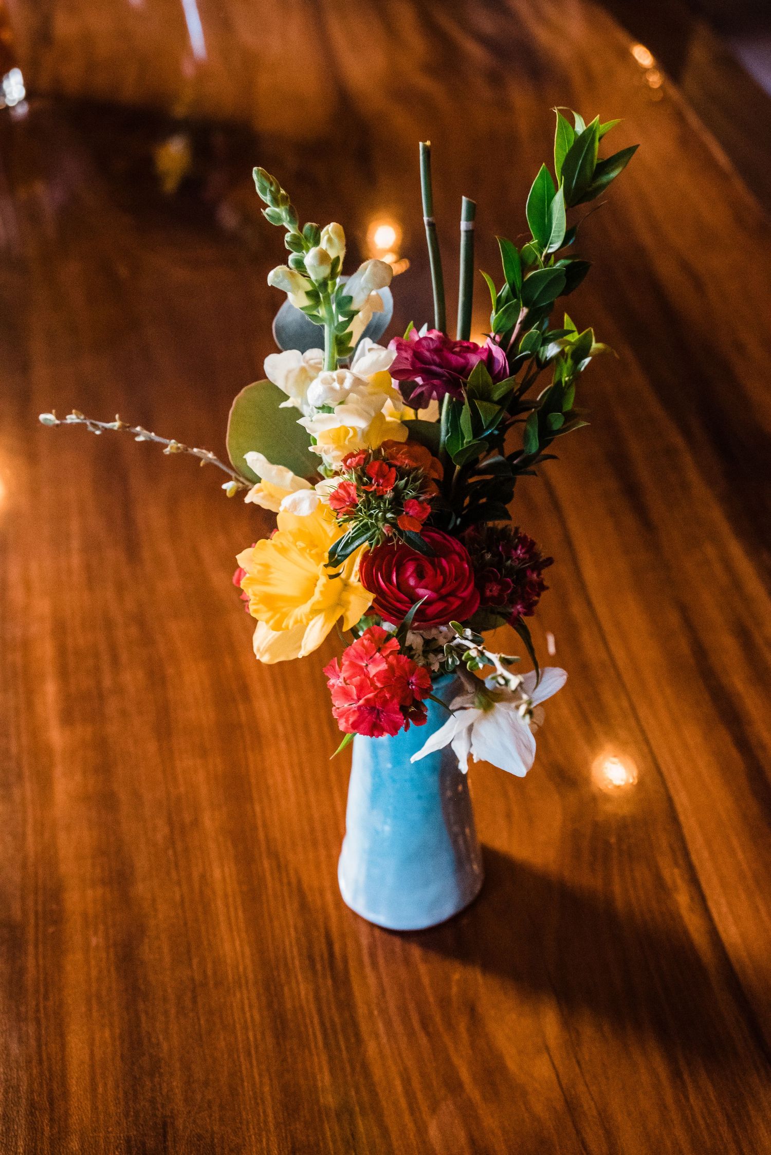 Colorful floral arrangement with yellow and red blooms in a blue vase on wooden surface.