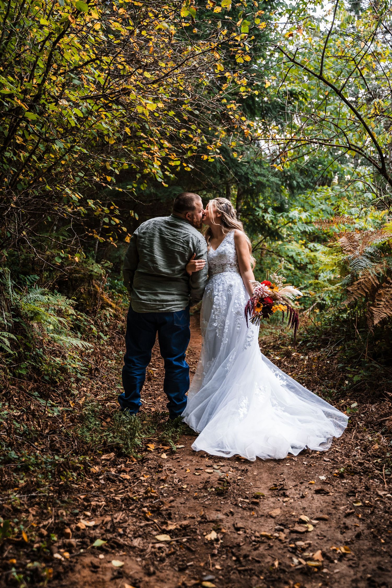 Couple walking down a forest path surrounded by autumn foliage.