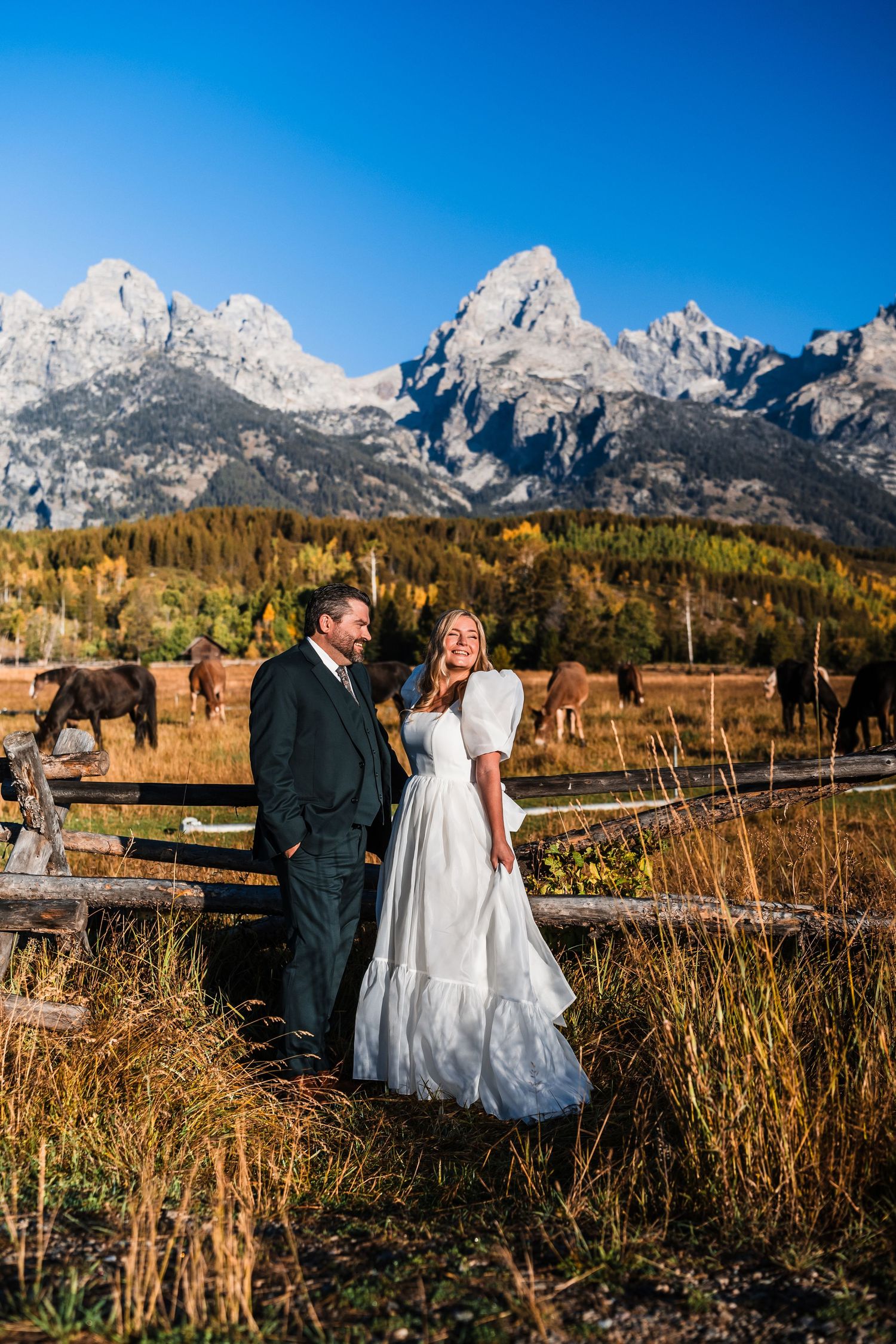 Newlyweds pose in front of majestic mountain peaks and autumn foliage at a rustic ranch.