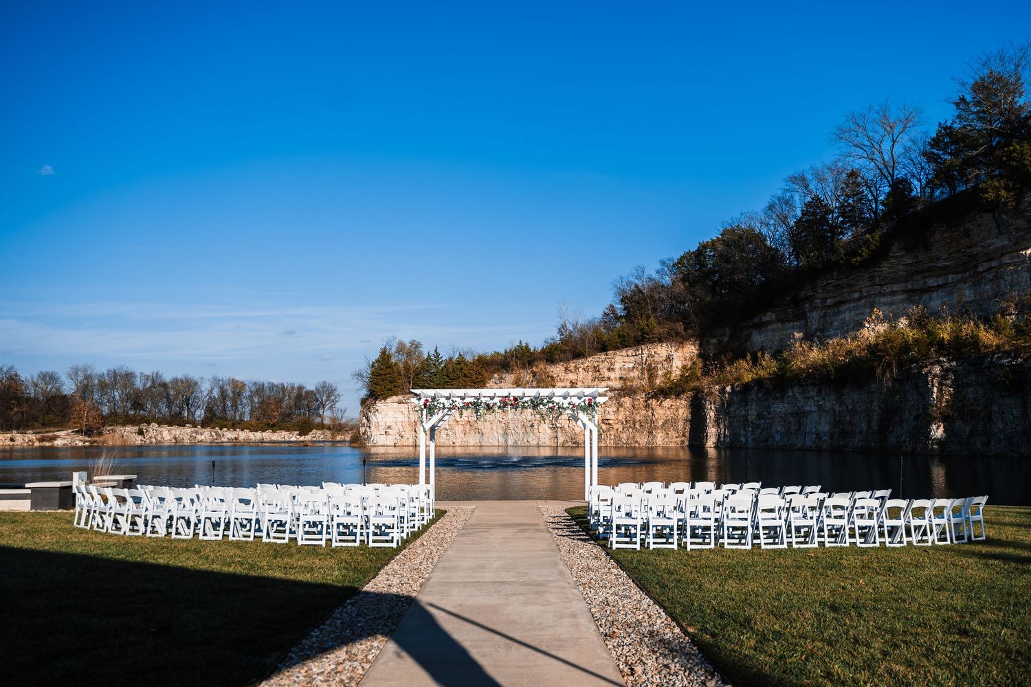 White chairs set up in rows for an outdoor wedding ceremony against a bright blue sky.