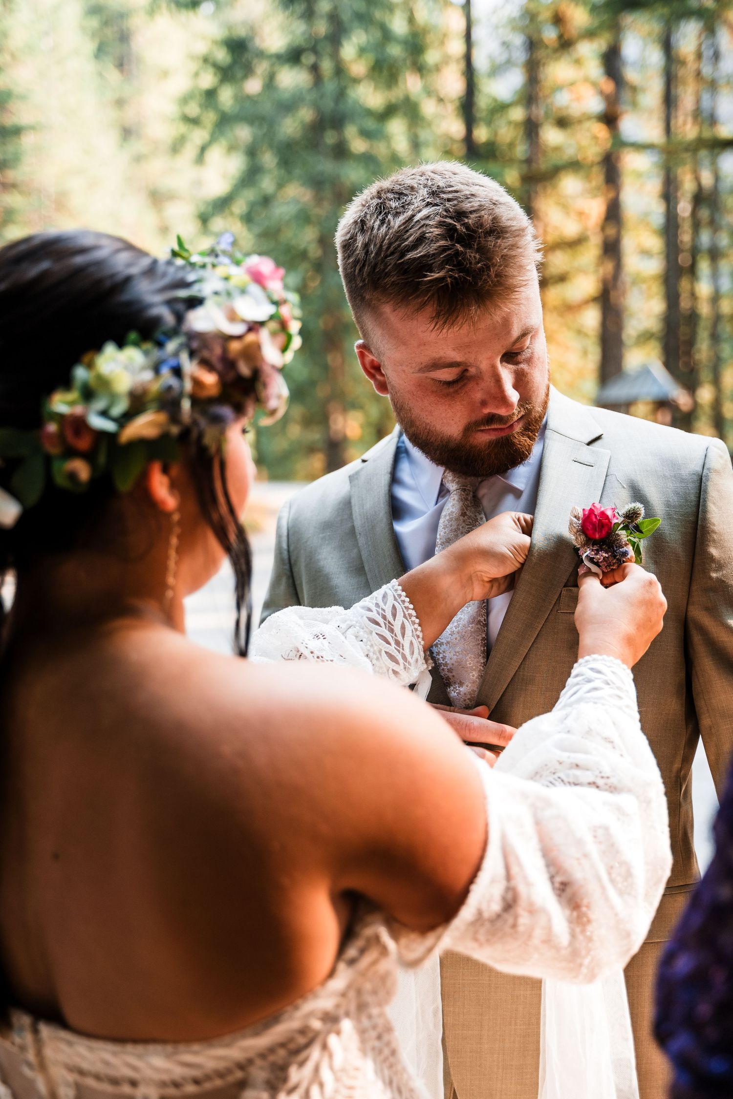 Intimate wedding moment in a sunlit forest with floral details and formal attire.