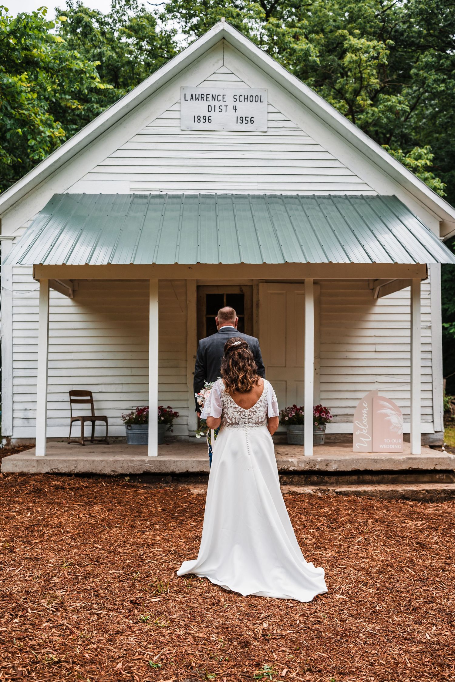 Couple entering historic white Lawrence School building with metal roof on mulch path.