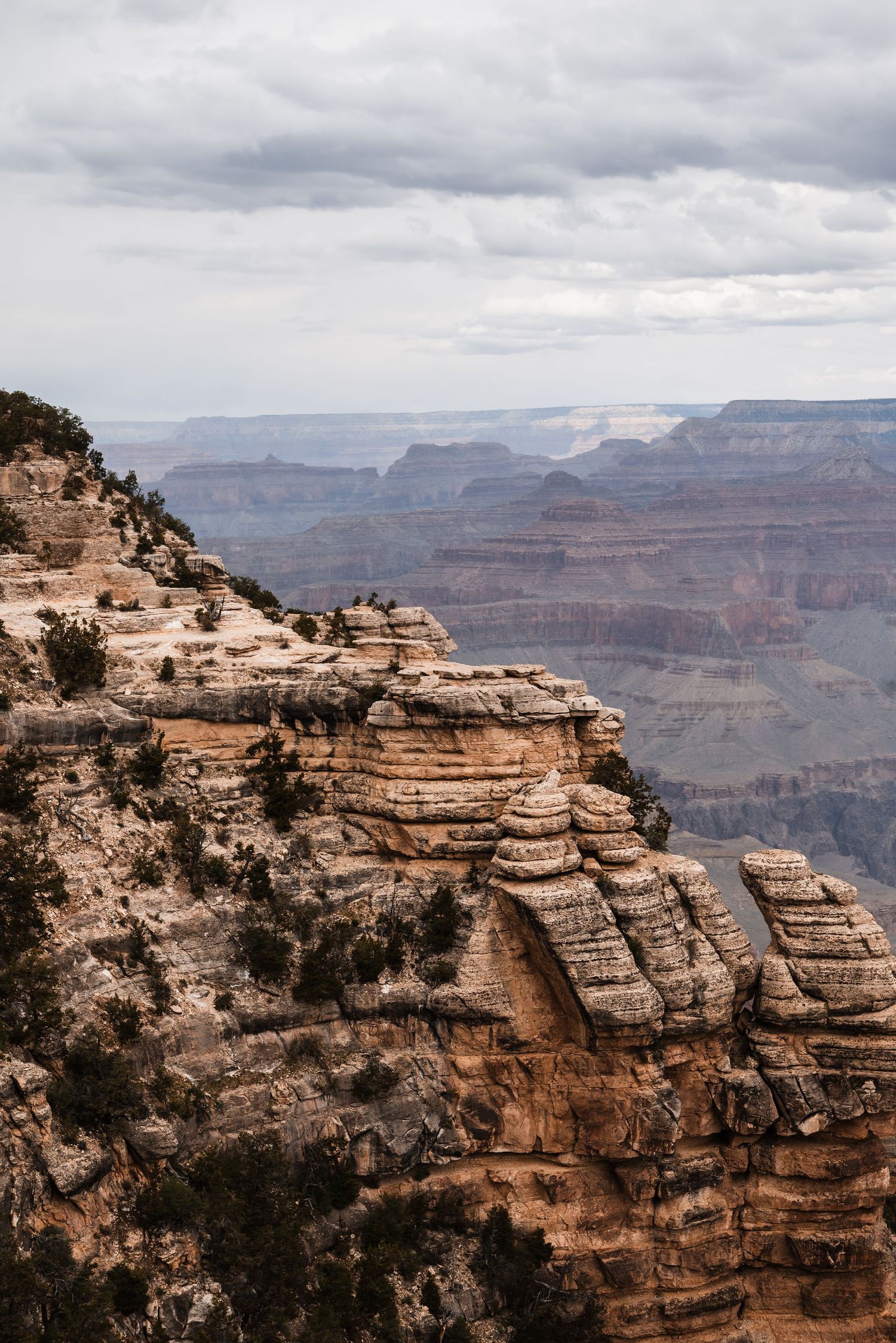 Layered rock formations and cliffs at the Grand Canyon with dramatic cloudy skies above.
