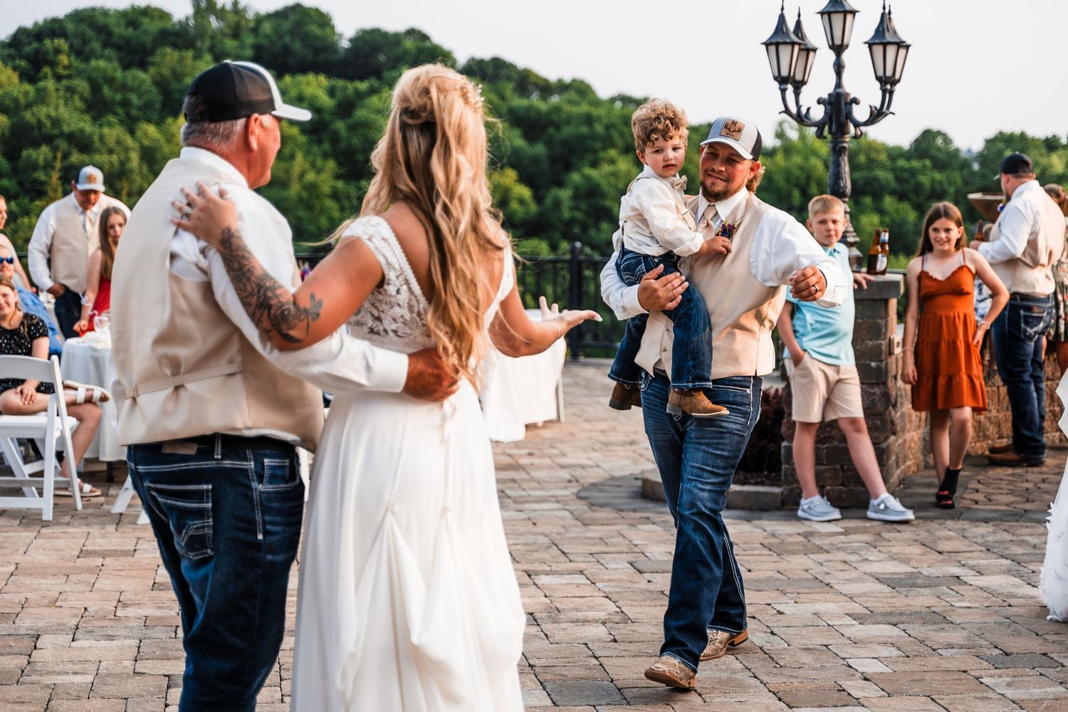 A couple share an intimate dance moment at an outdoor wedding reception on a stone patio.