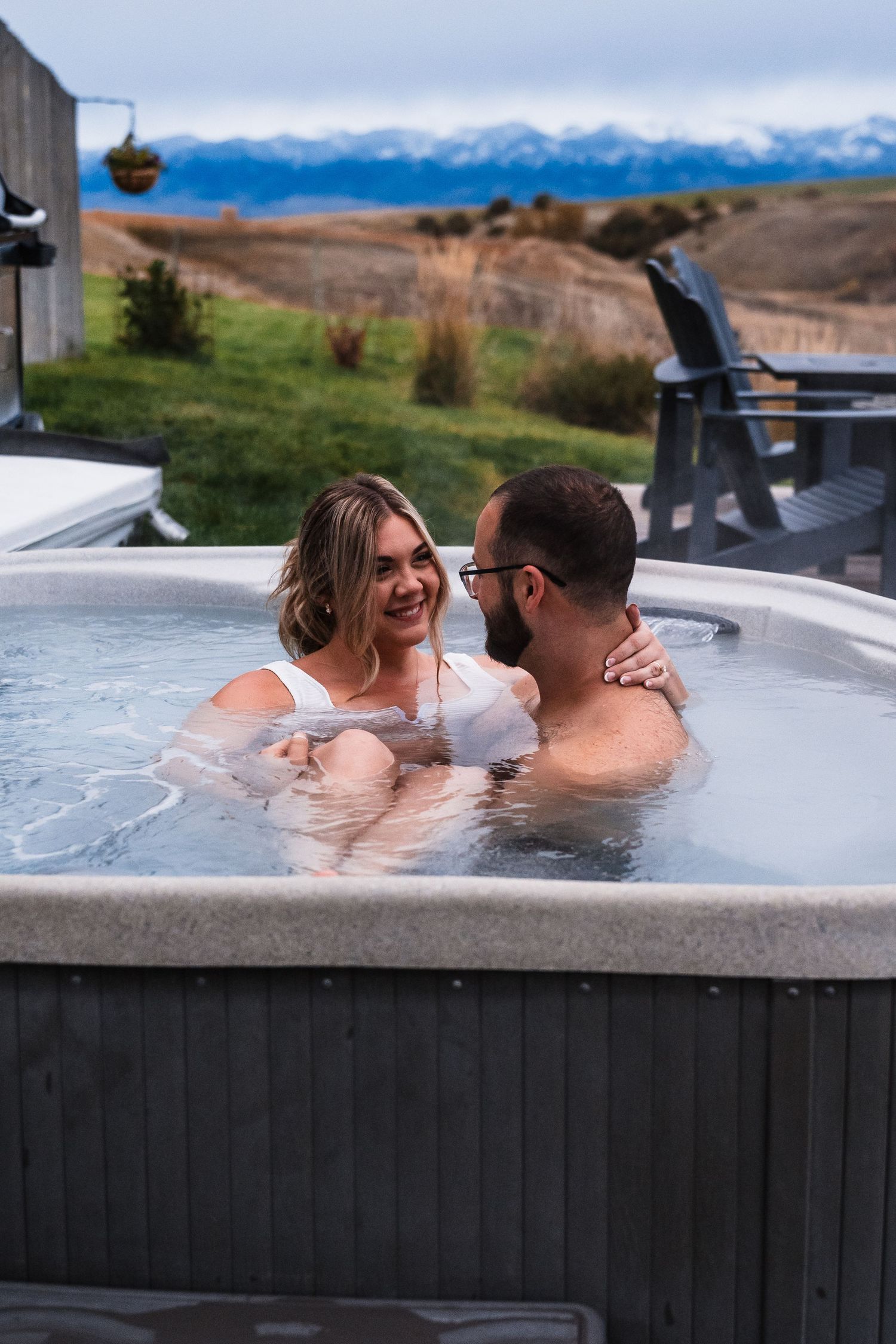 A couple enjoys a relaxing soak in an outdoor hot tub with scenic mountain views in the background.