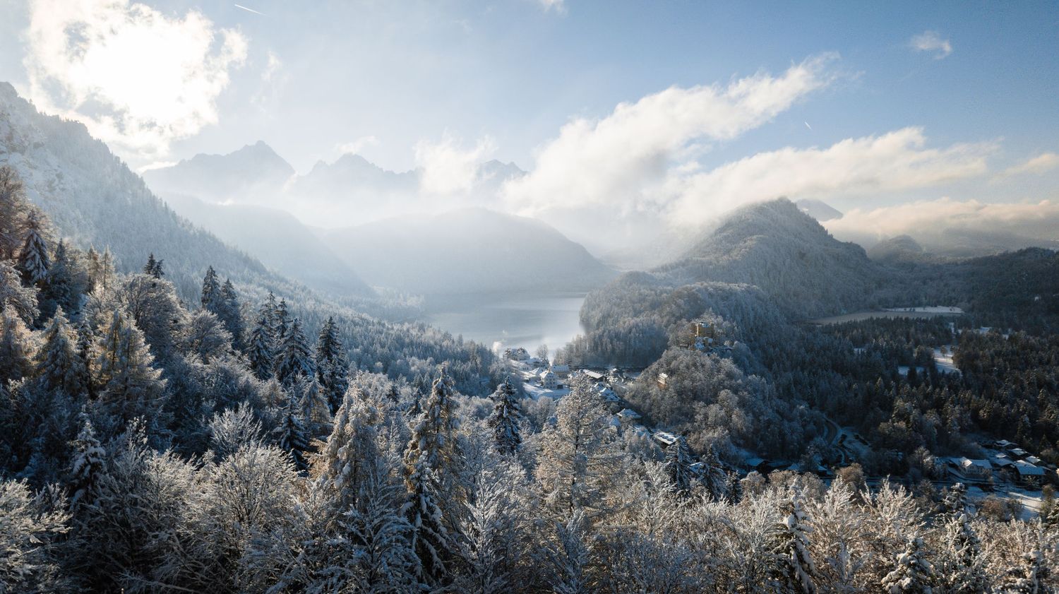 Panoramic winter mountain landscape with snow-covered peaks and cloudy sky.