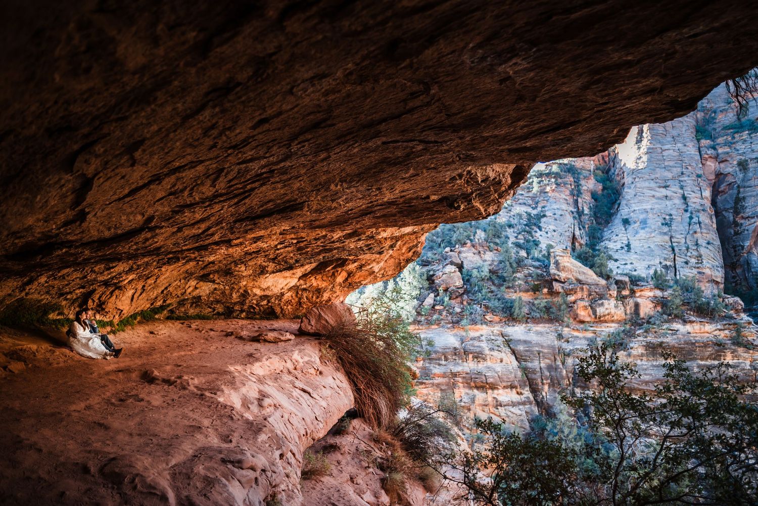 Bride sitting peacefully inside dramatic sandstone cave alcove at Zion National Park.