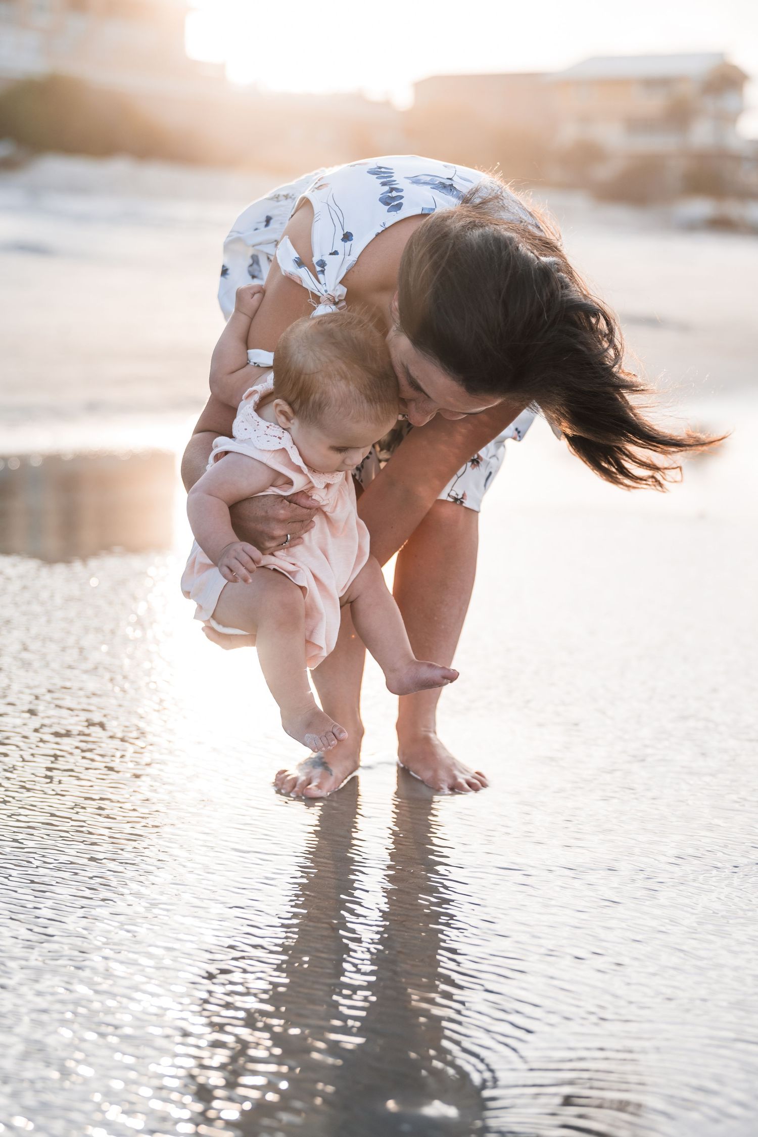 Parent and child playing in shallow beach water at sunset creating a dreamy silhouette effect.