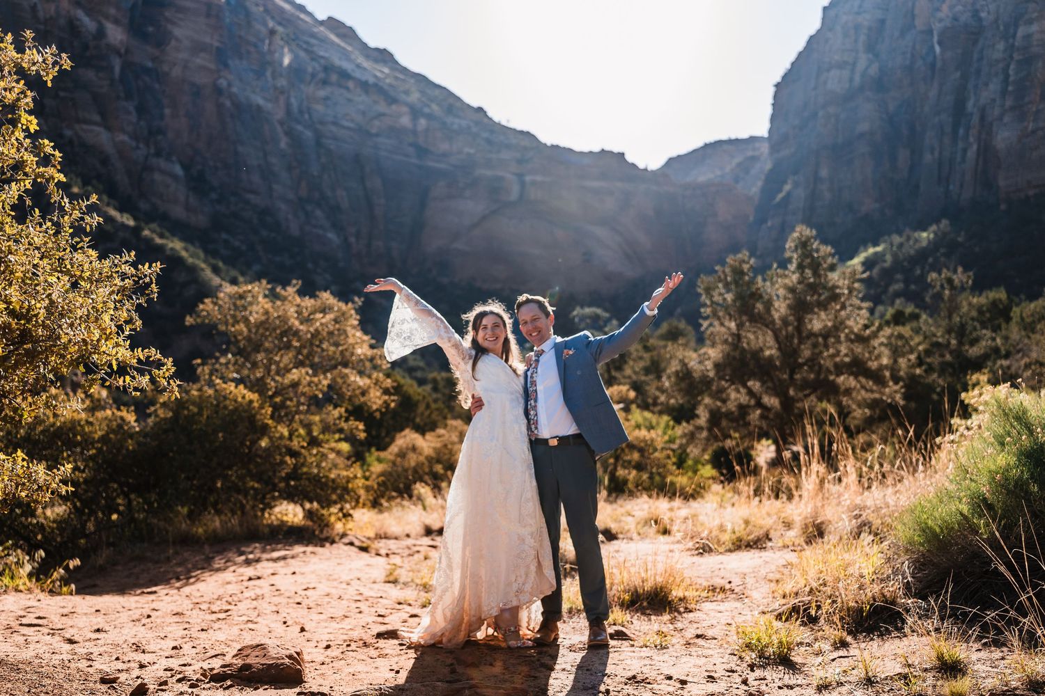 Happy wedding couple celebrating elopement with arms raised in Zion National Park canyon.