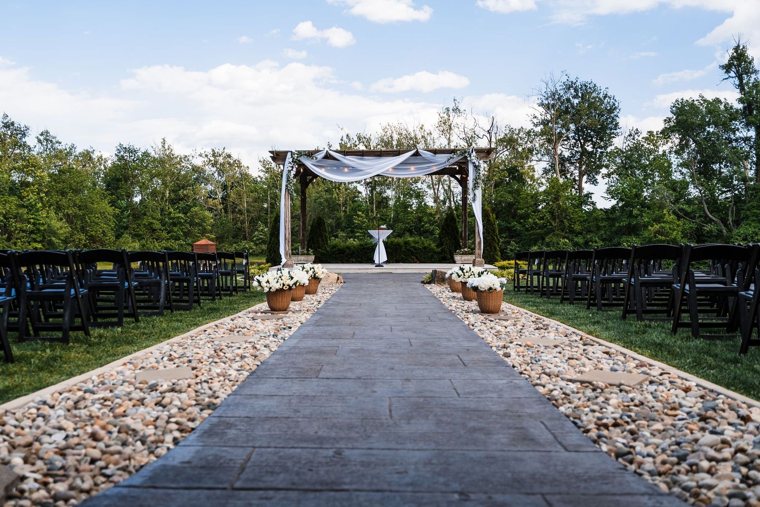 Outdoor wedding ceremony aisle lined with rocks leading to a draped wooden arch.