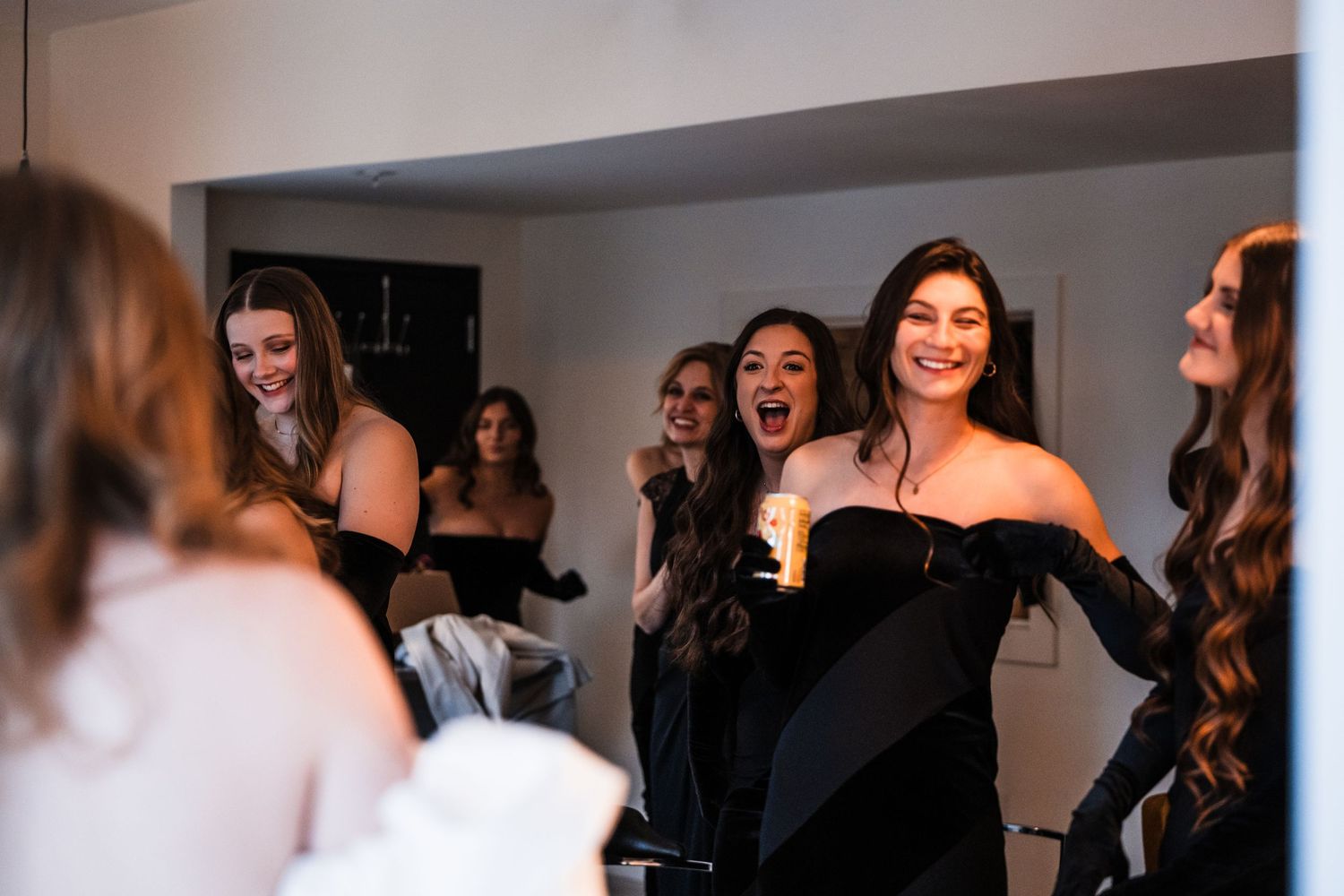Bridesmaids in black dresses react with excitement during wedding preparations.