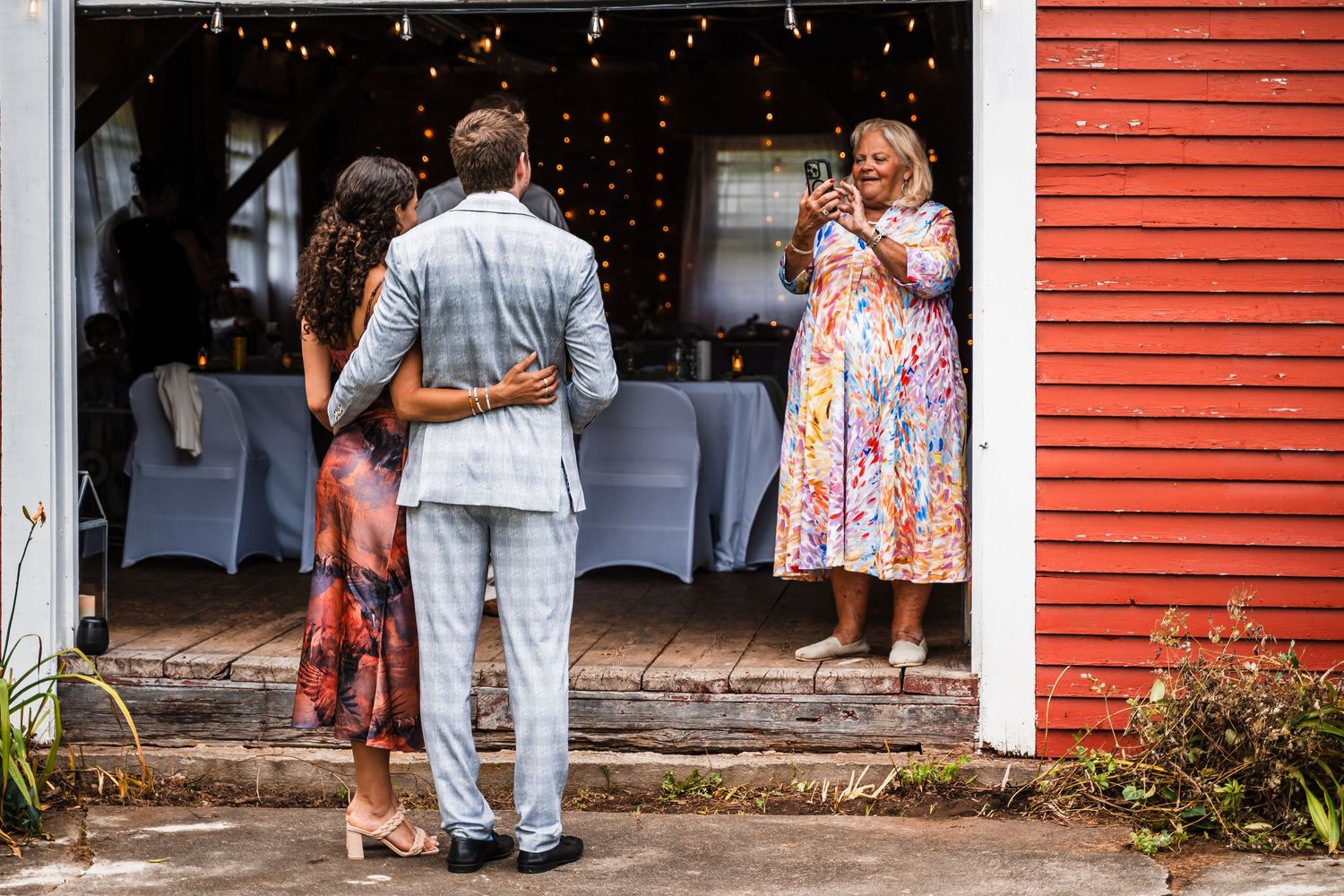 Guests arriving at a rustic red barn venue decorated with string lights.