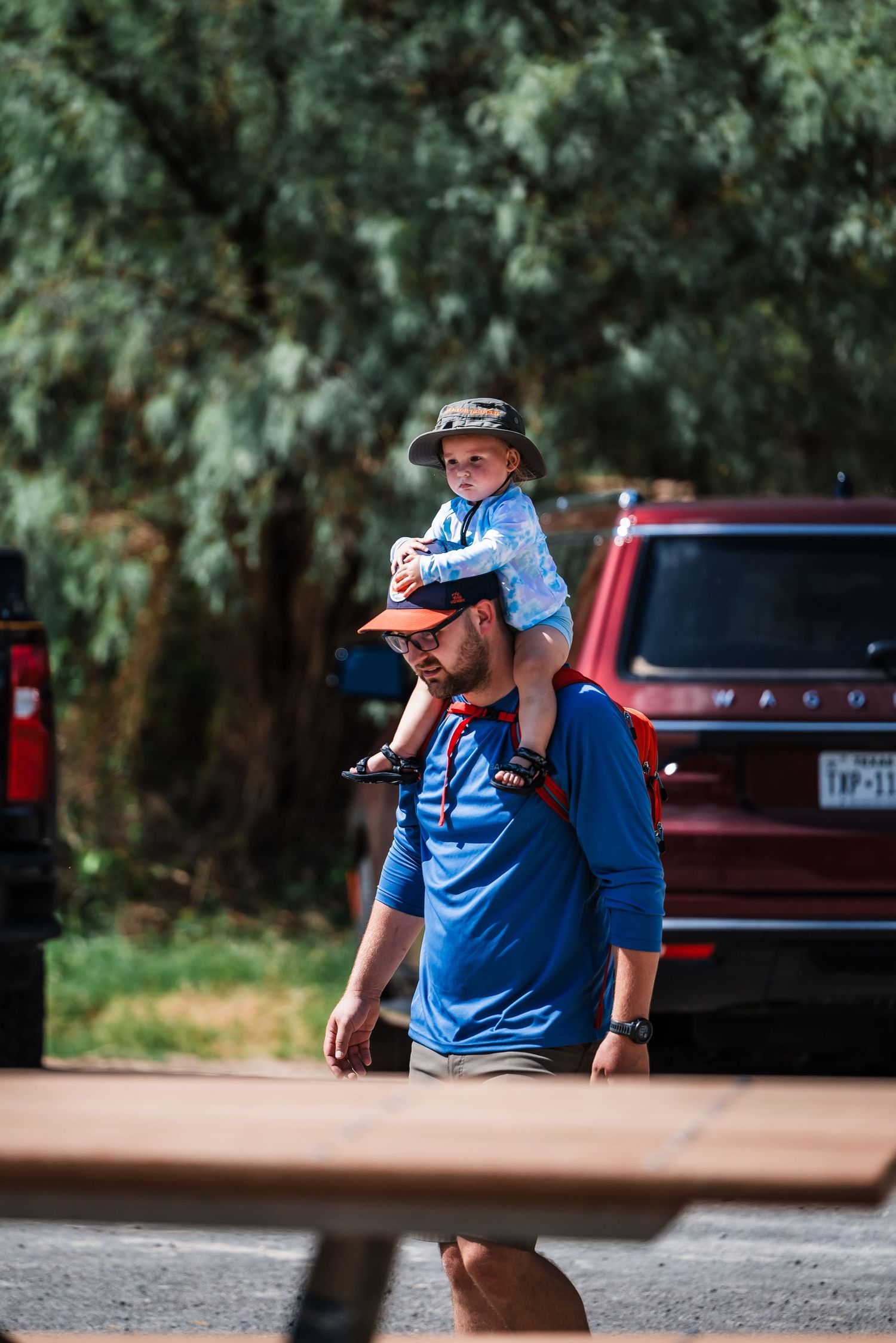 A shoulder ride through a park on a sunny day with trees and a red truck in the background.