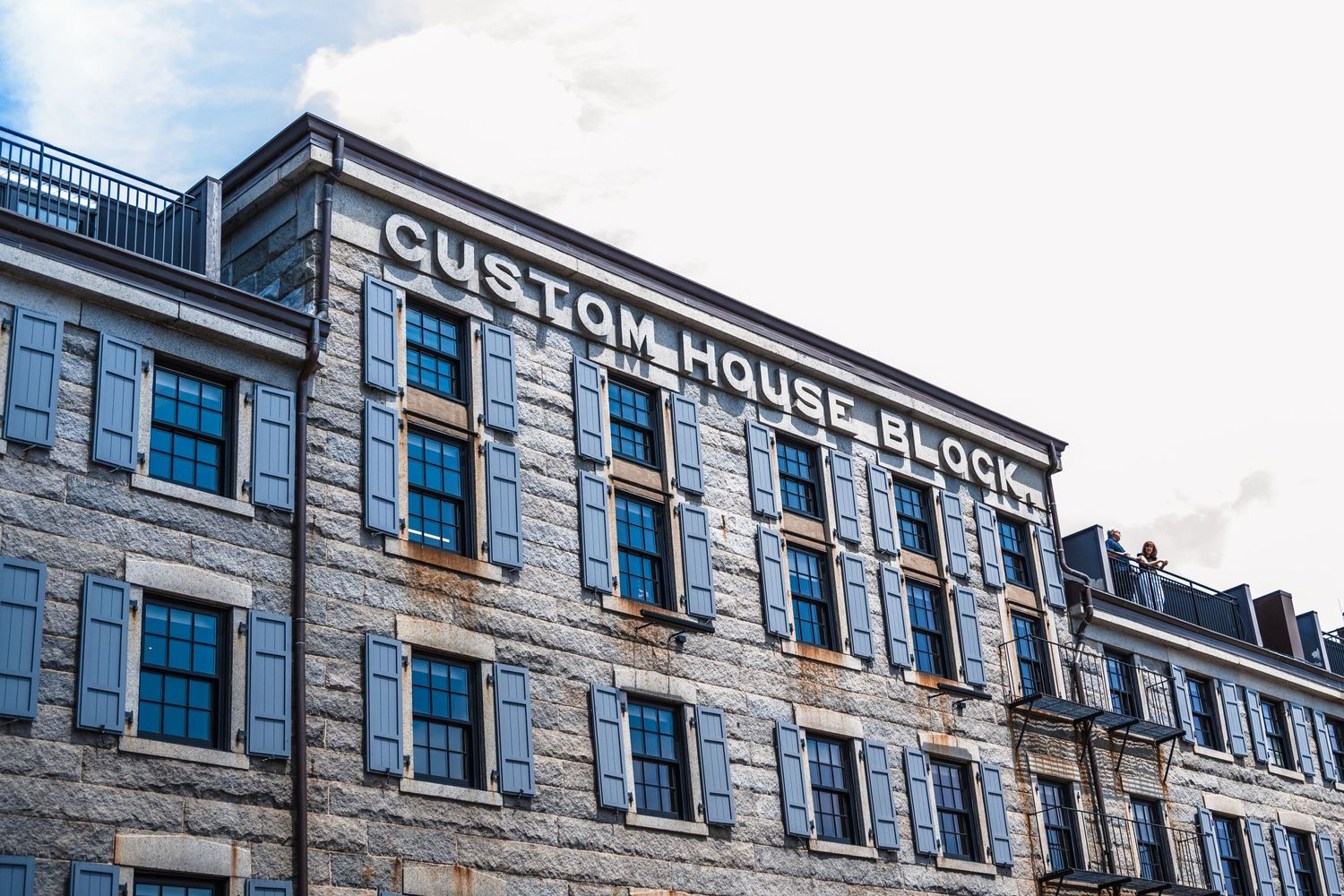 Historic Custom House Block building facade with stone architecture and blue windows against cloudy sky.