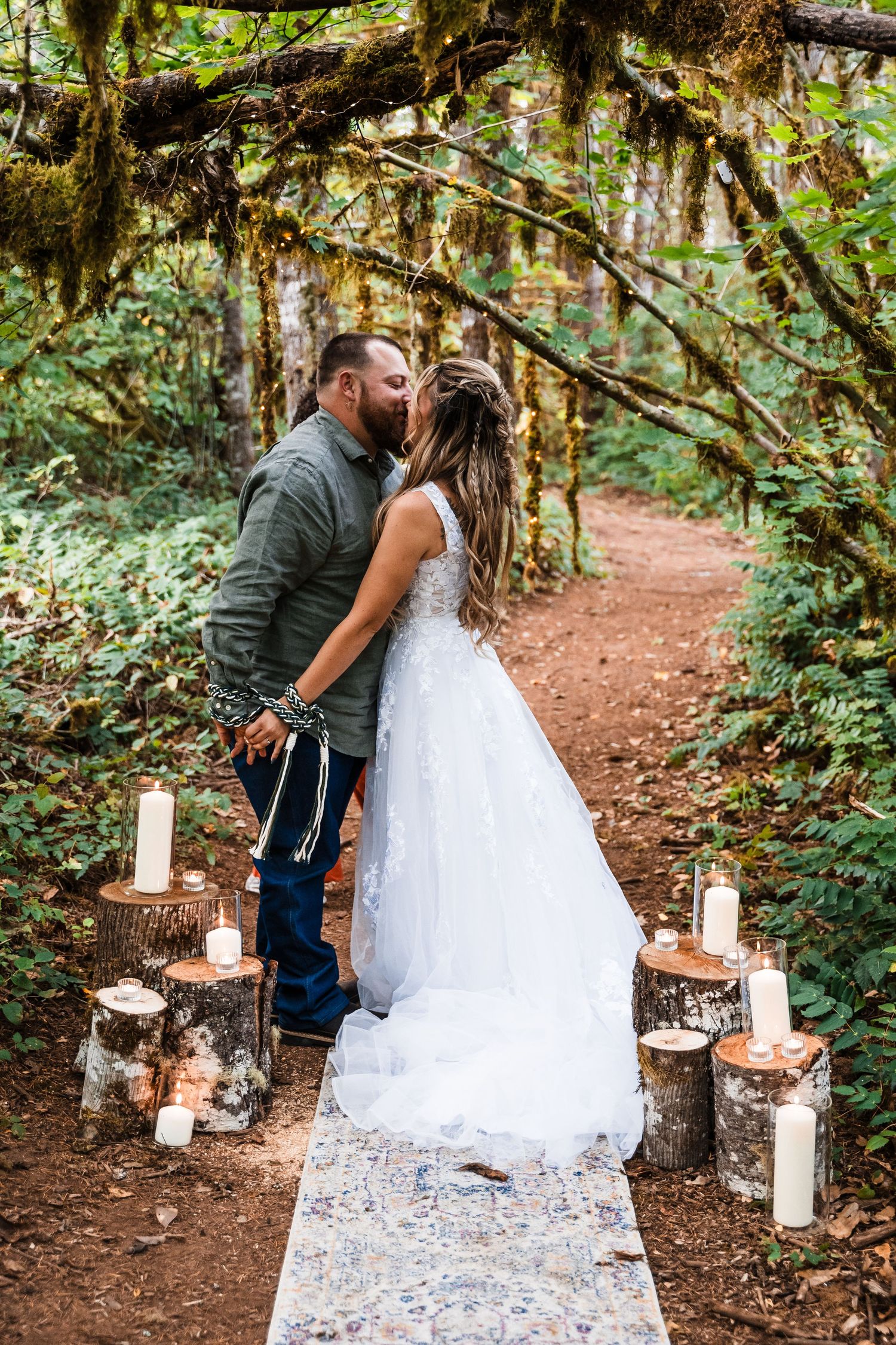 Romantic forest wedding moment on decorated trail with candles and moss-draped trees.