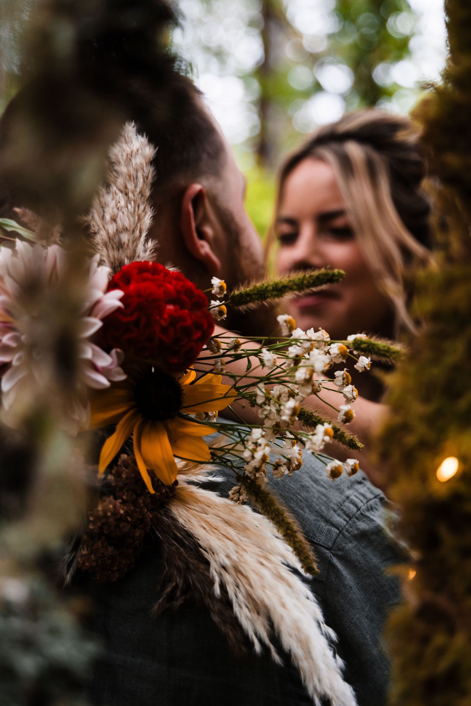 Wedding bouquet with red flowers and pampas grass in a forest setting.