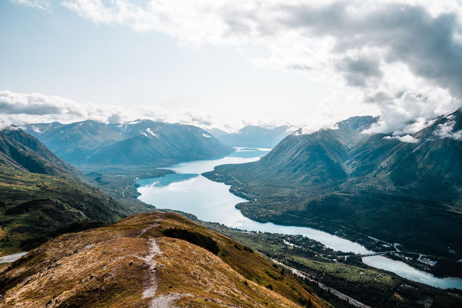 Aerial view of winding turquoise lakes surrounded by snow-capped mountains and rugged terrain in a dramatic Alaskan landscape.