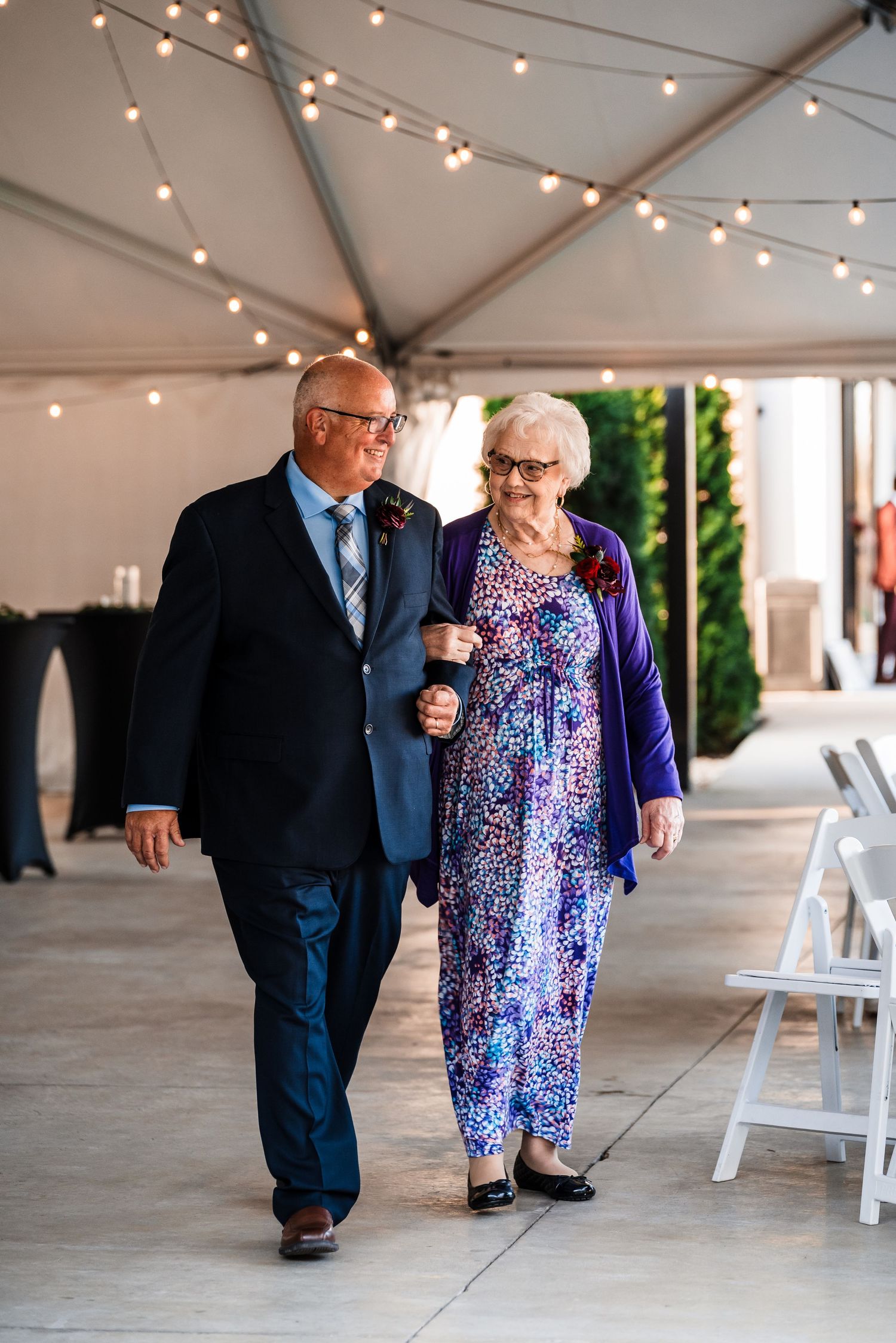 String lights illuminate a covered walkway where an elderly couple walks together.