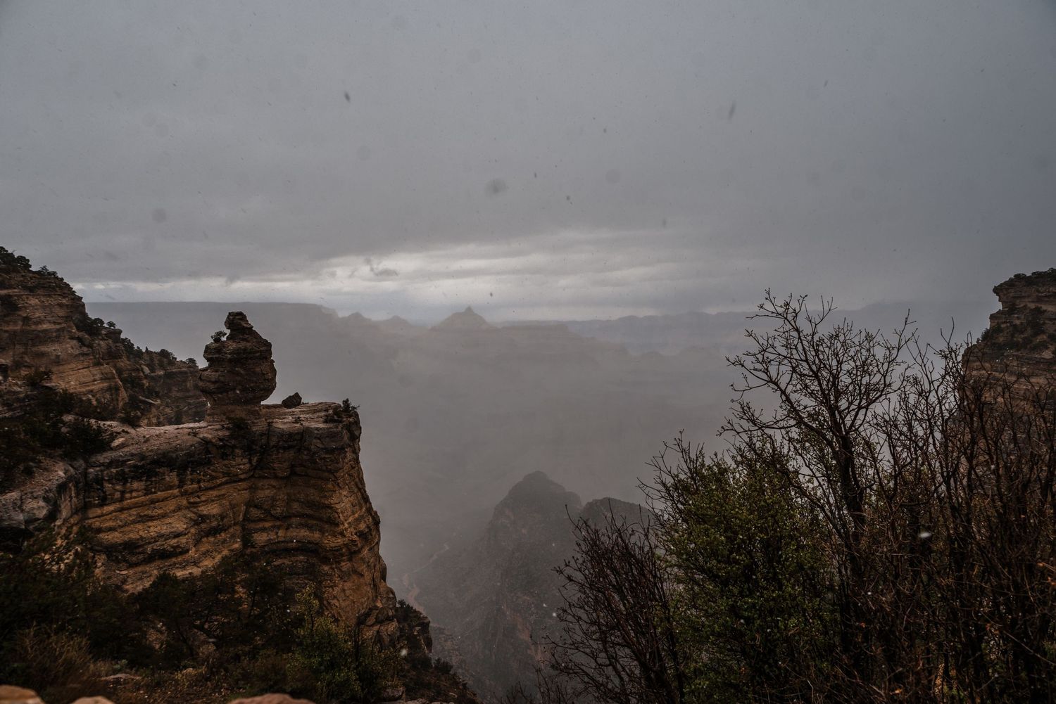 A moody view of the Grand Canyon's rocky cliffs shrouded in storm clouds and fog.