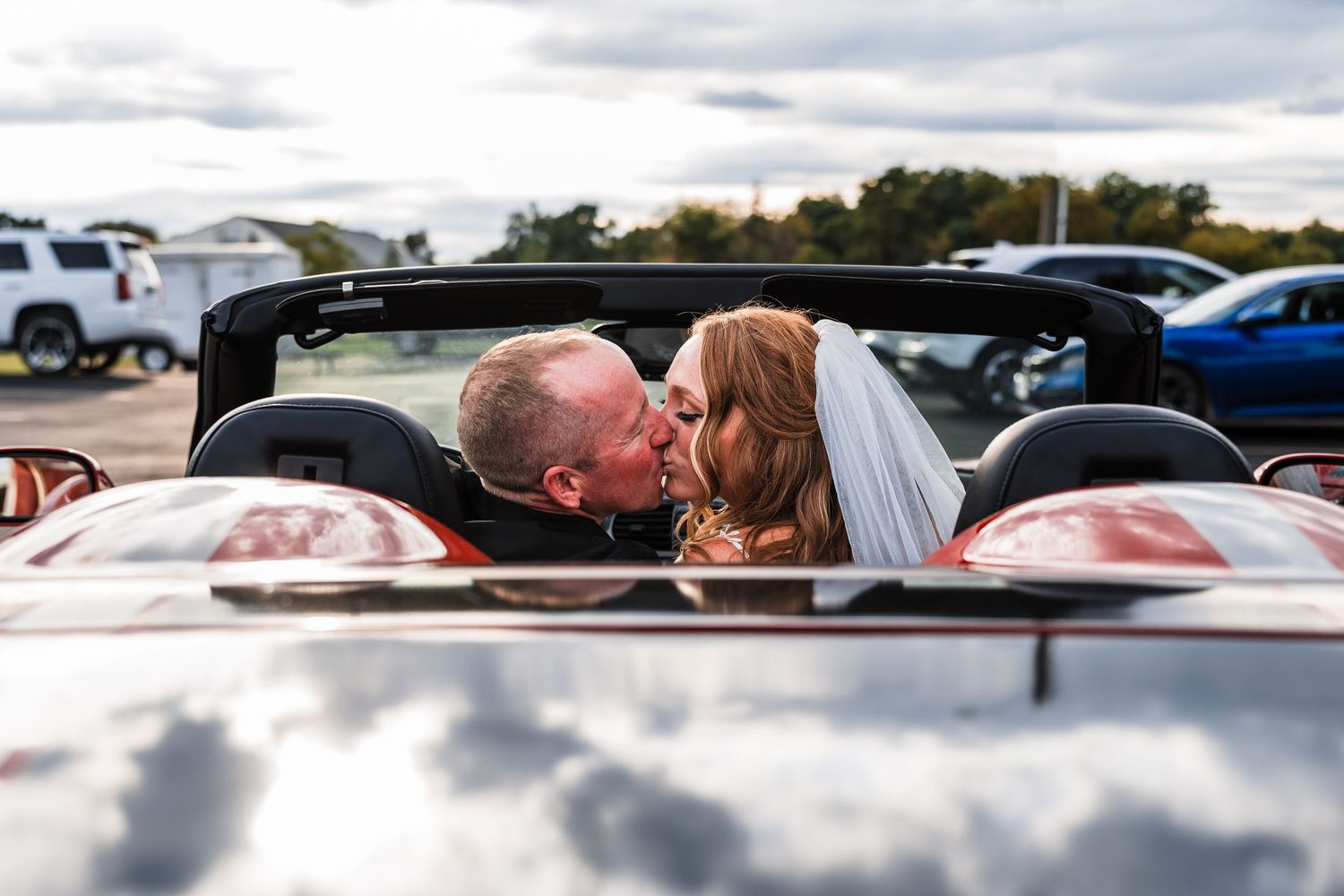 Wedding party vehicles parked under cloudy skies at outdoor venue.