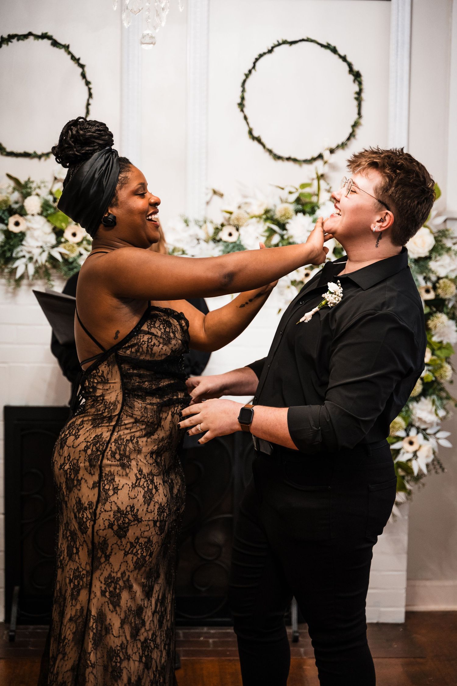A couple sharing a joyful moment in front of decorative floral wreaths at their wedding celebration.