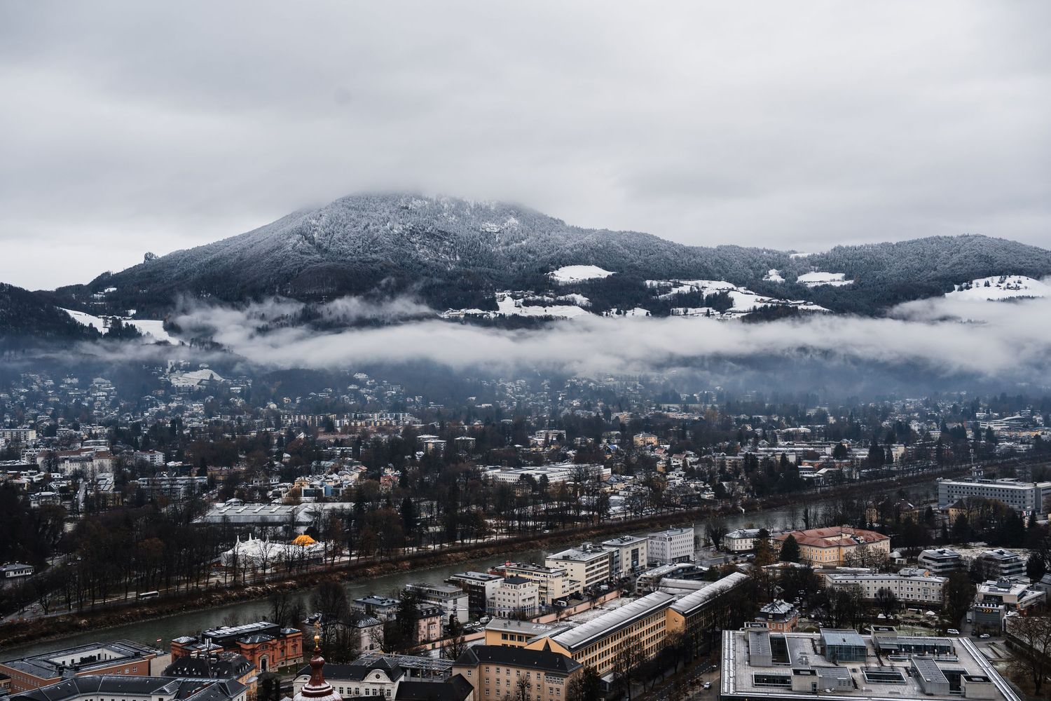 Panoramic winter view of a mountain town with snow-capped peaks in the background.