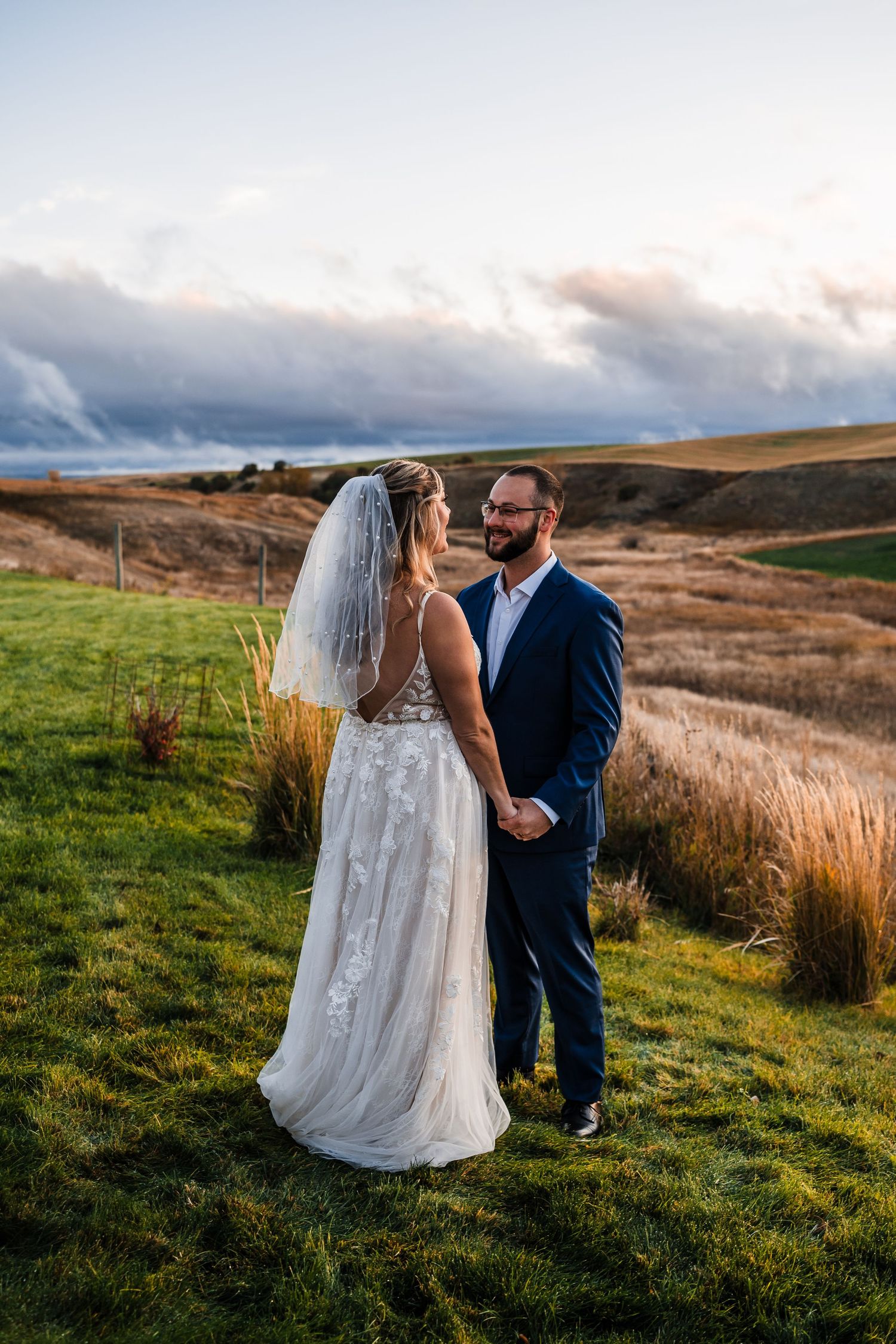 A couple in wedding attire shares an intimate moment on a grassy hilltop during golden hour.