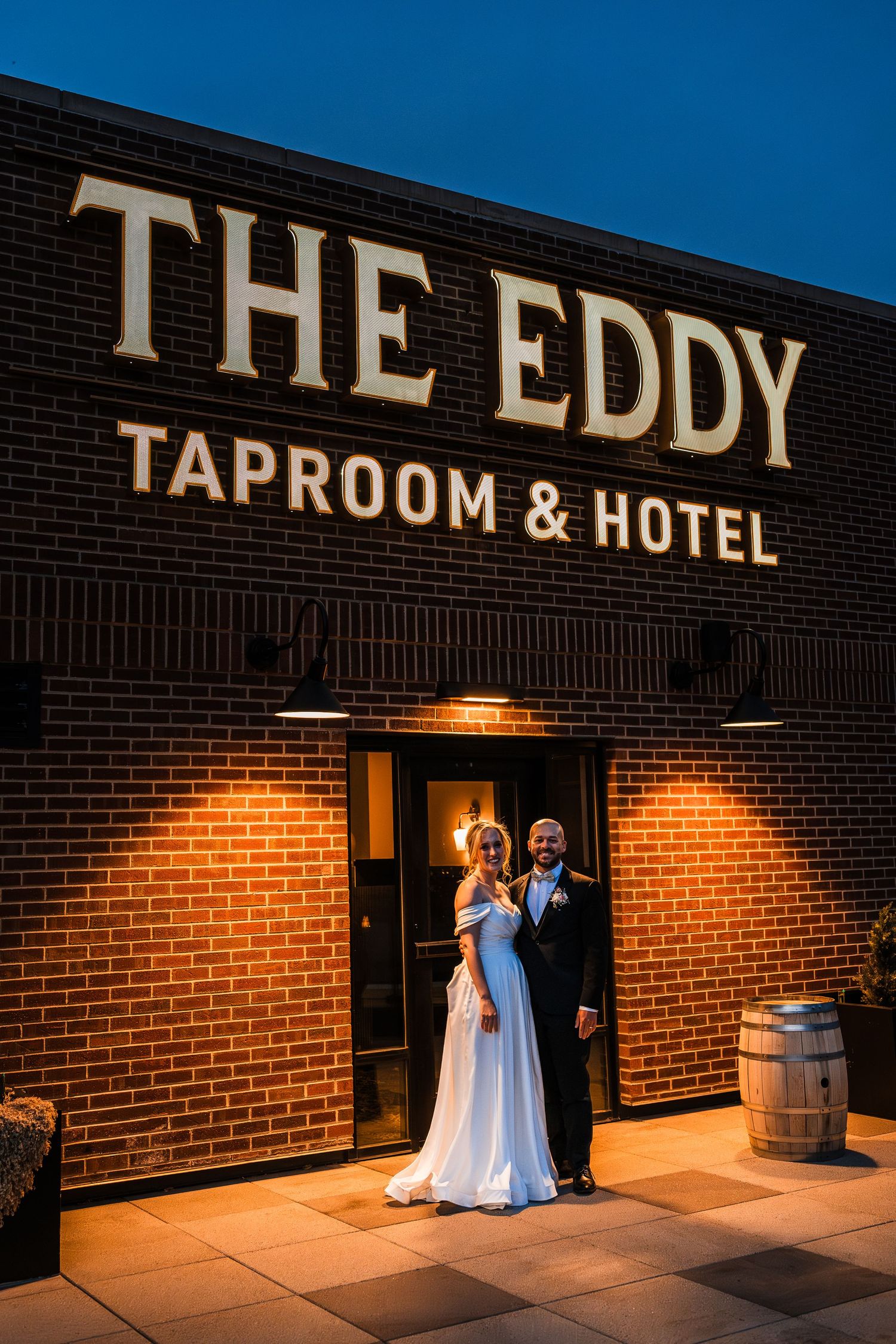 Newlyweds posing at night outside The Eddy Taproom and Hotel, bride in white gown and groom in suit.