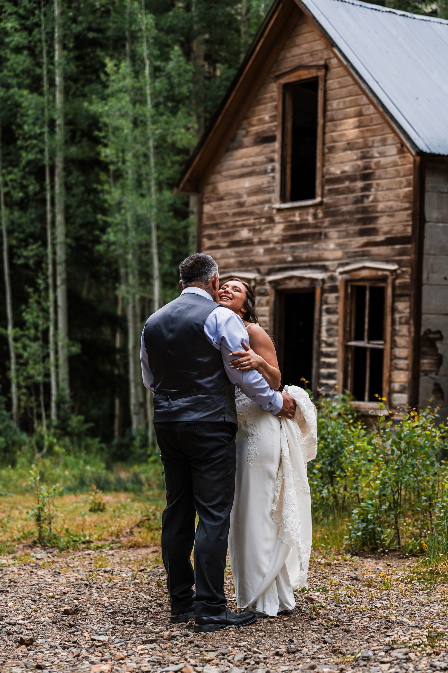 Newlyweds embracing near a rustic abandoned cabin in a Colorado aspen forest setting.