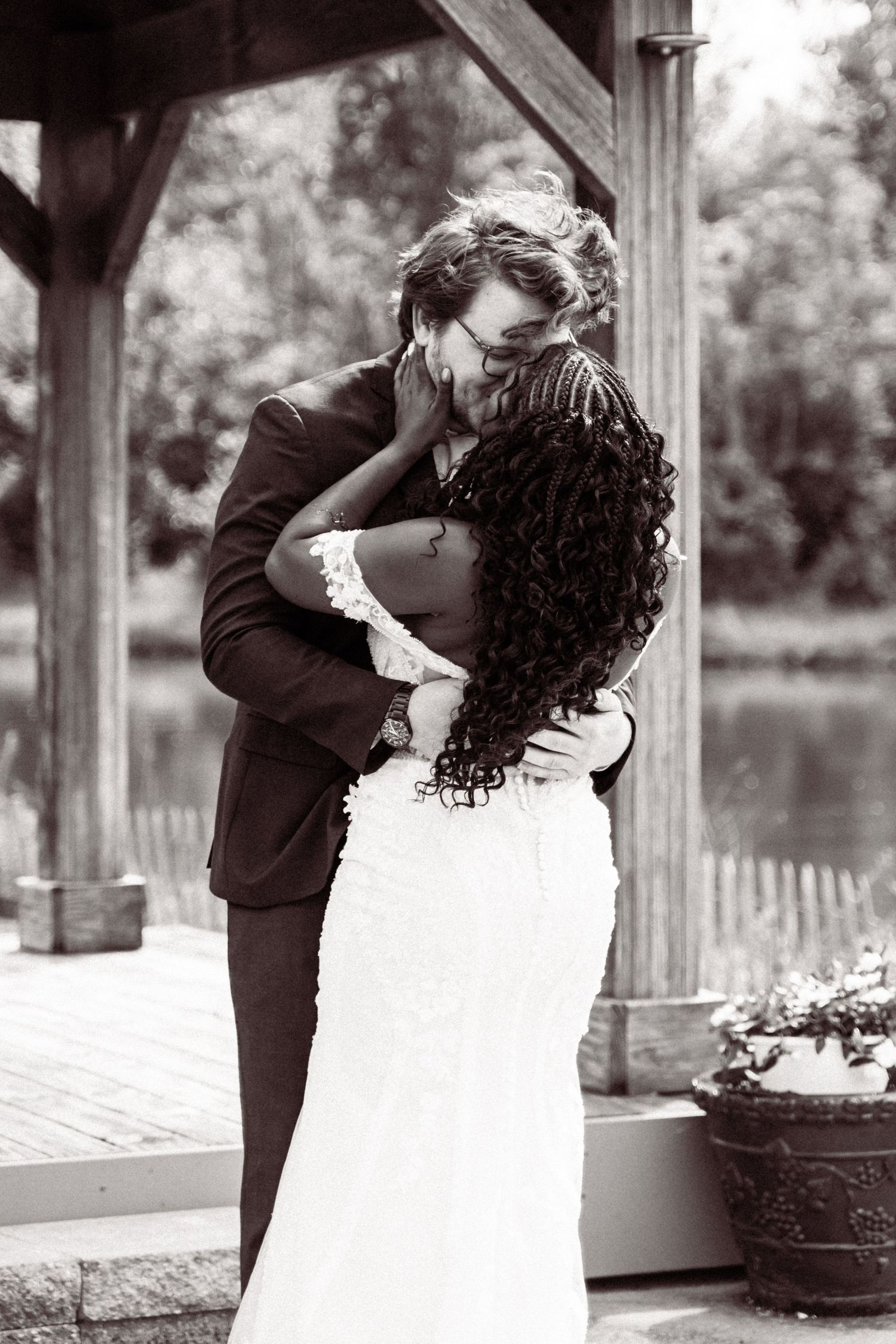 Bride and groom share a romantic kiss under a wooden pergola in a black and white wedding portrait.